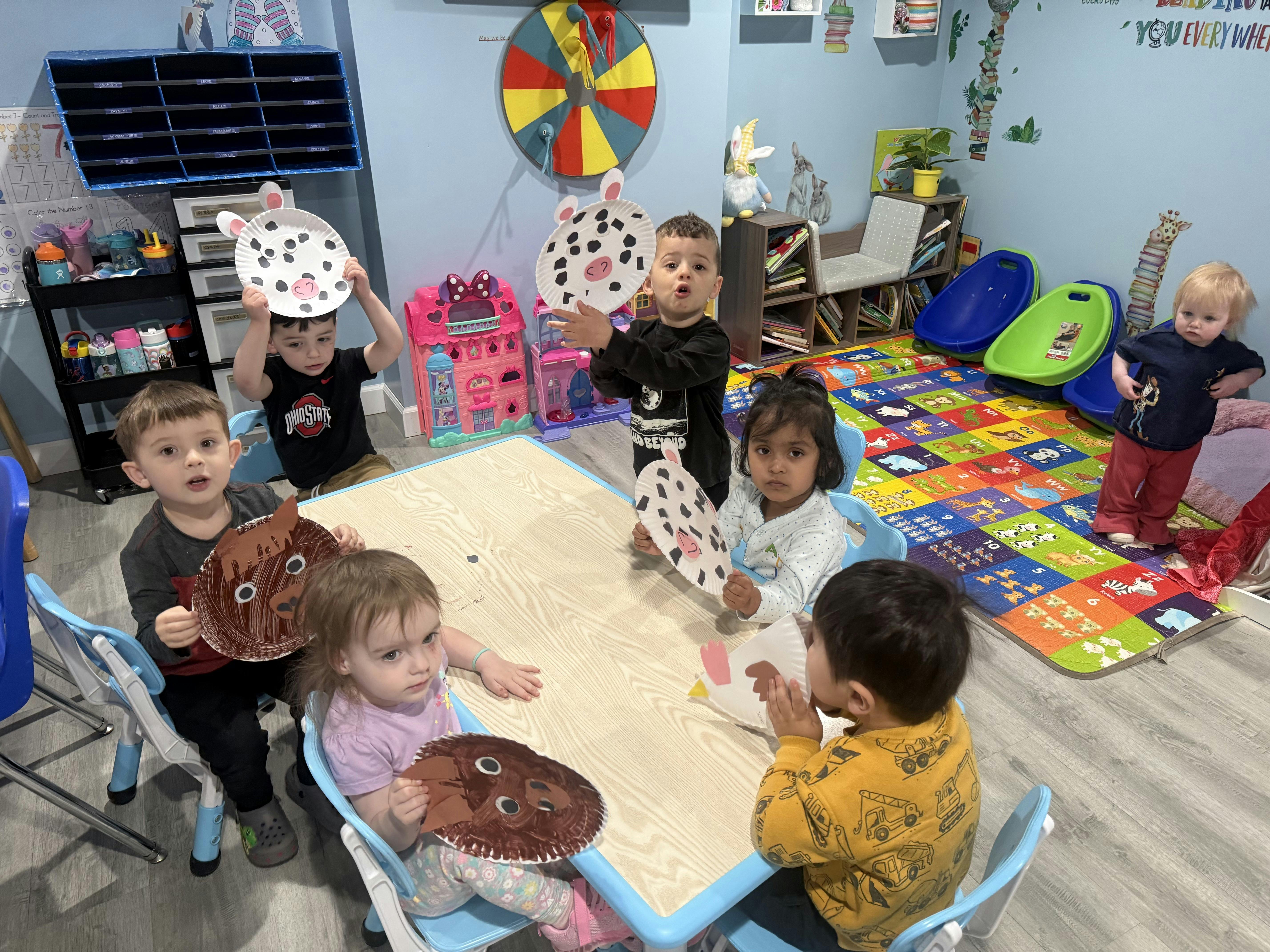 Several young children at a table holding up paper plate animal crafts