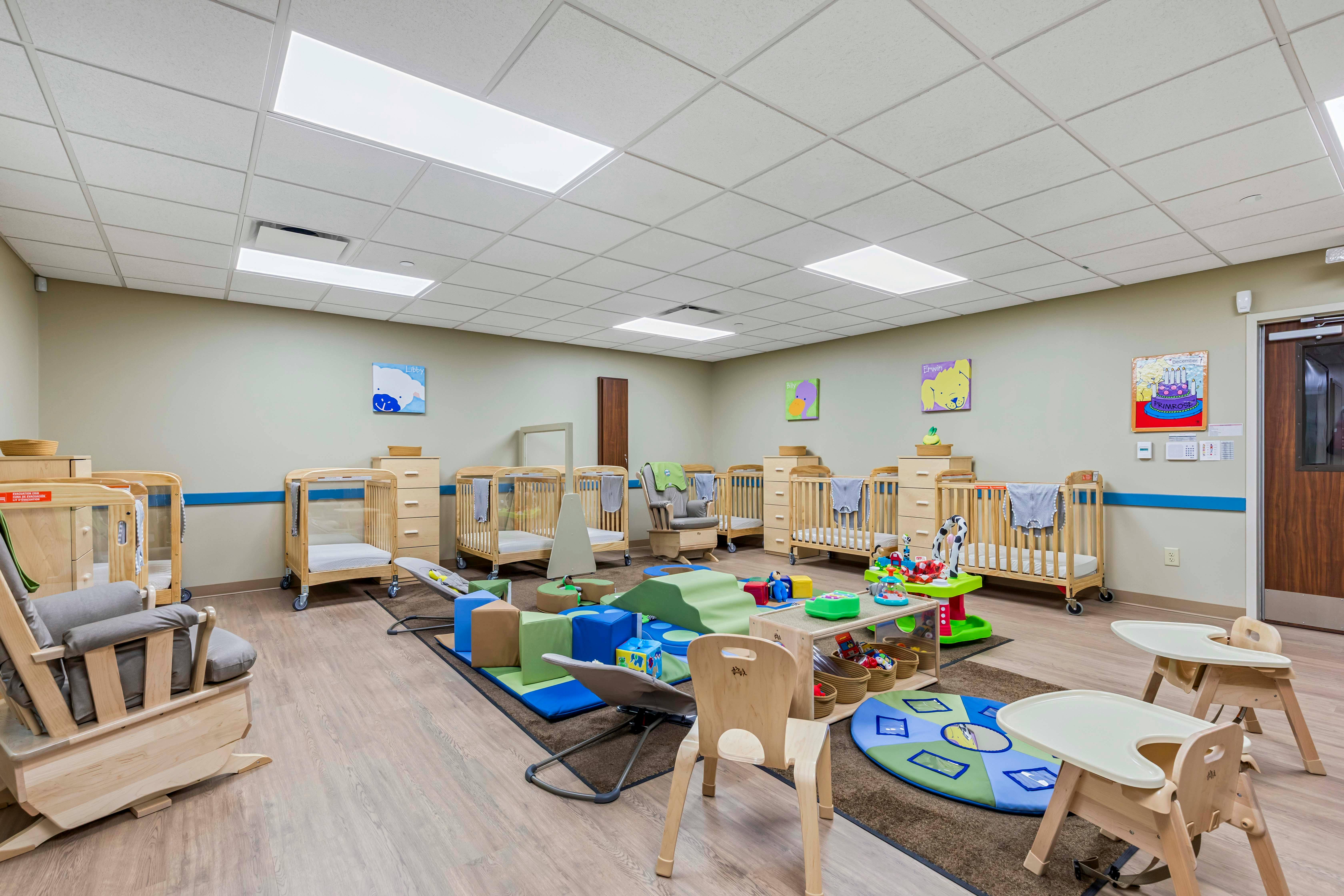 Classroom with multiple cribs, a rocking chair, soft play equipment, and high chairs