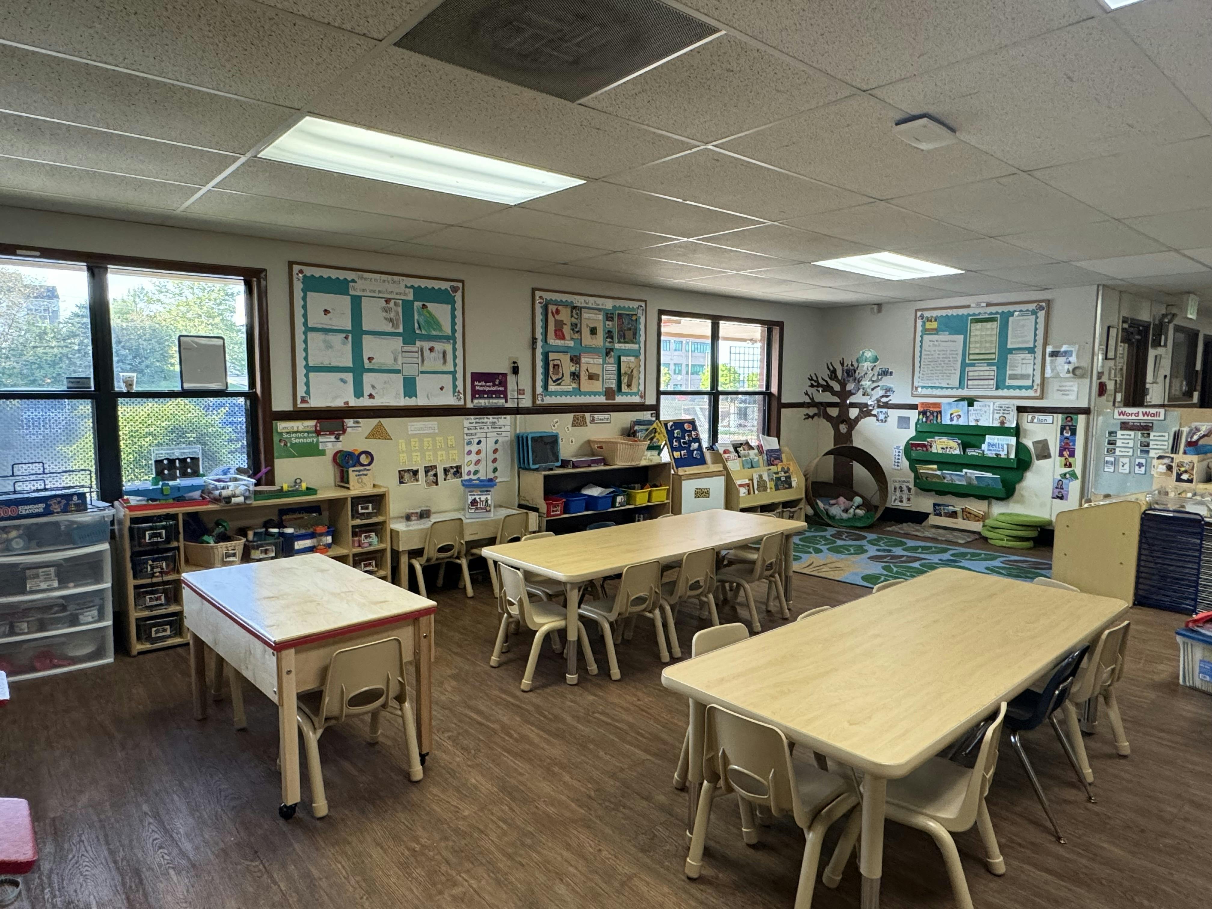 Empty classroom with small tables and chairs, windows, and educational posters on the walls