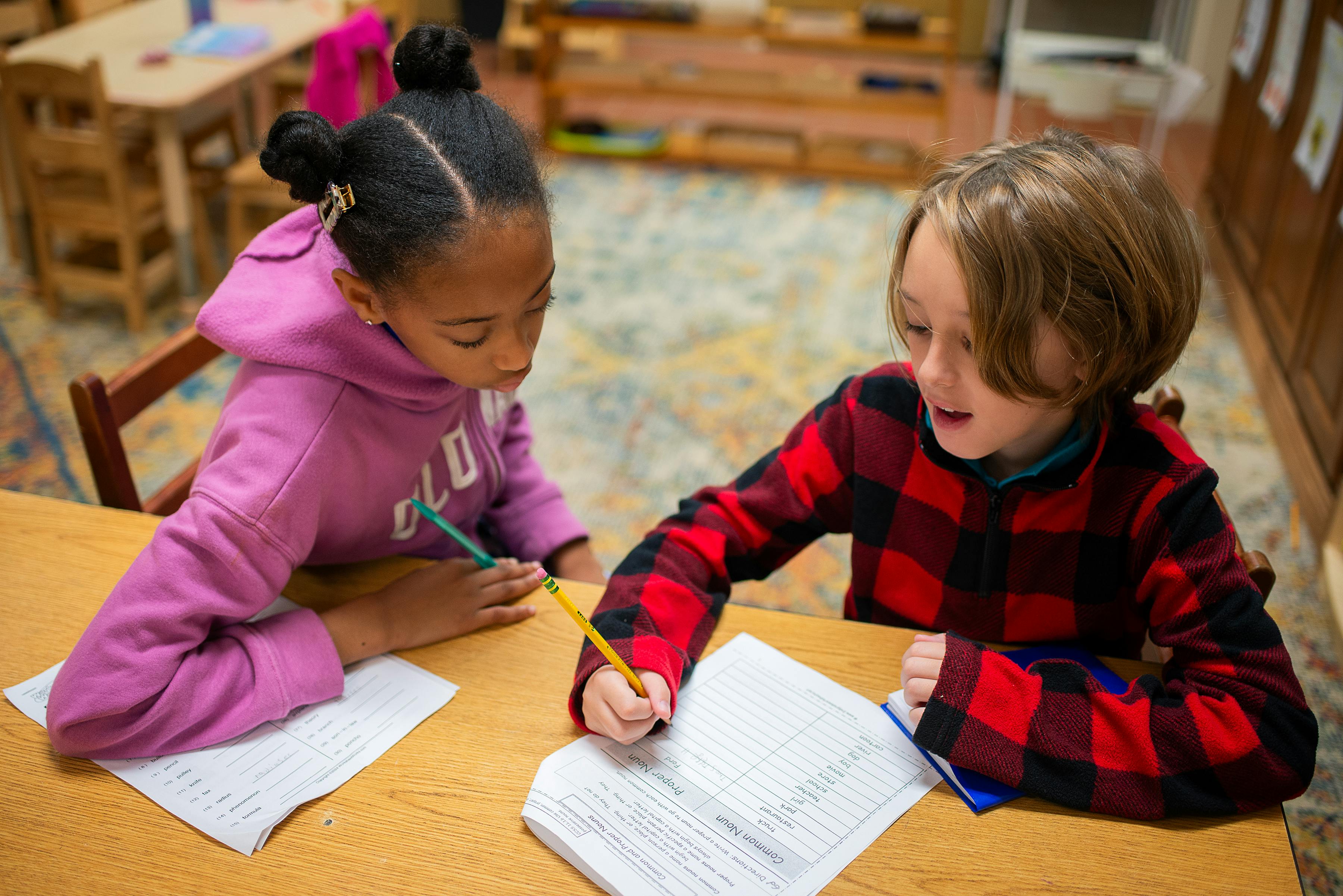 Two children writing in notebooks at a table