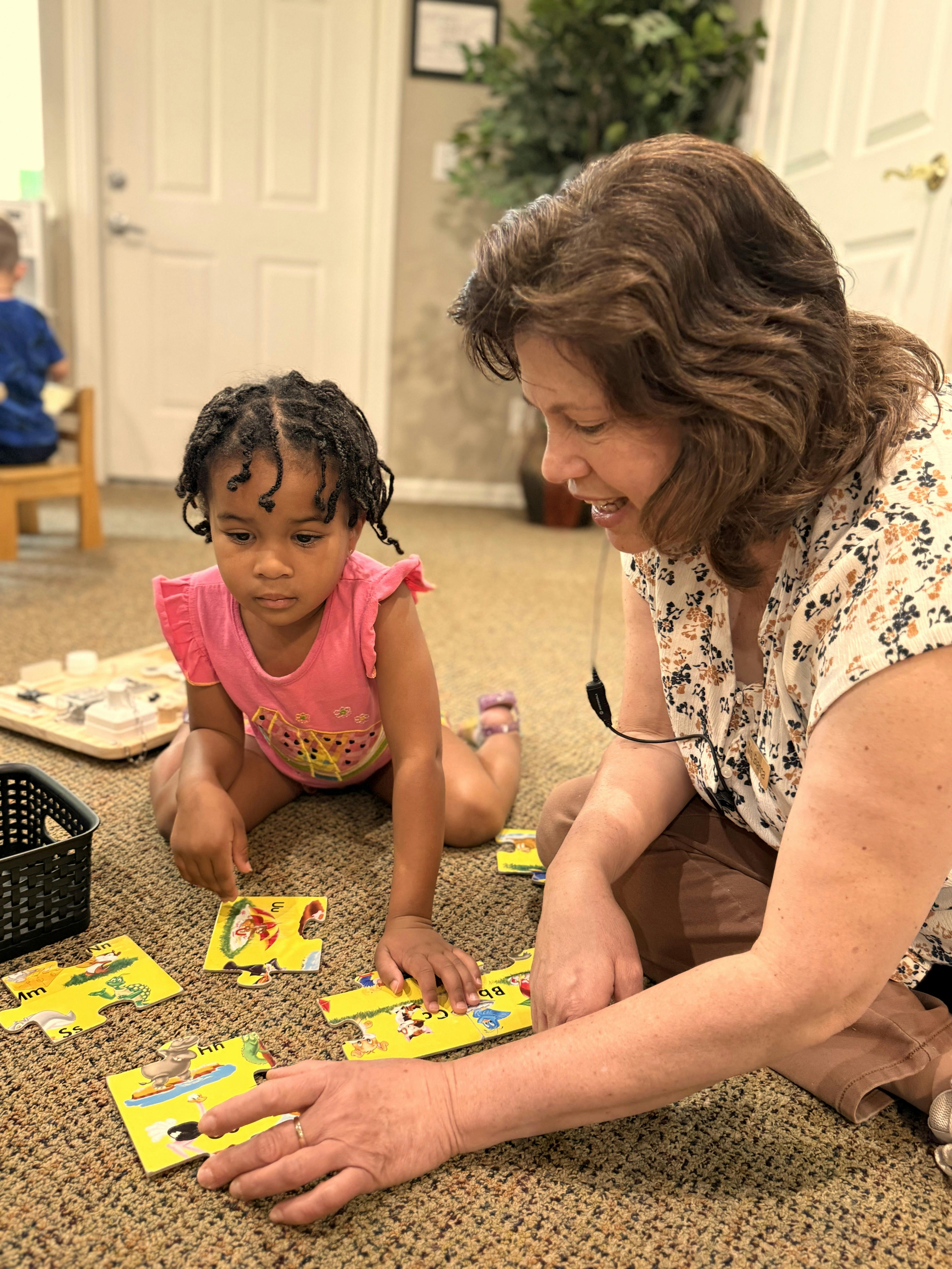 Adult and child playing with alphabet puzzle pieces on the floor