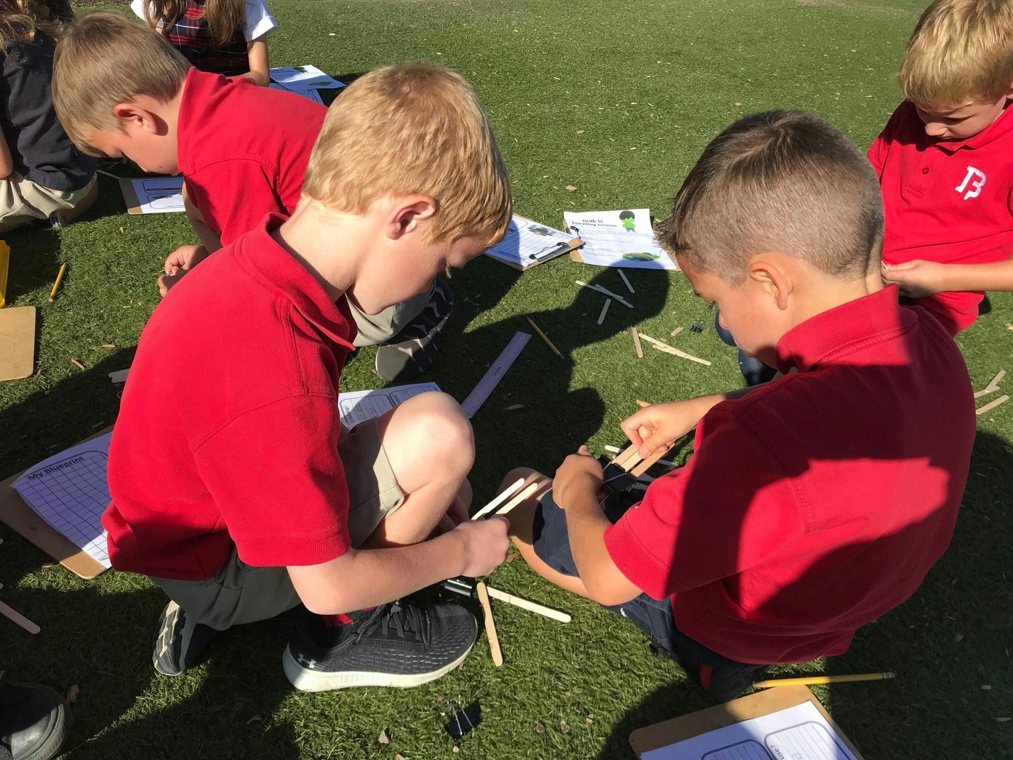 Children in red shirts building with craft sticks outdoors