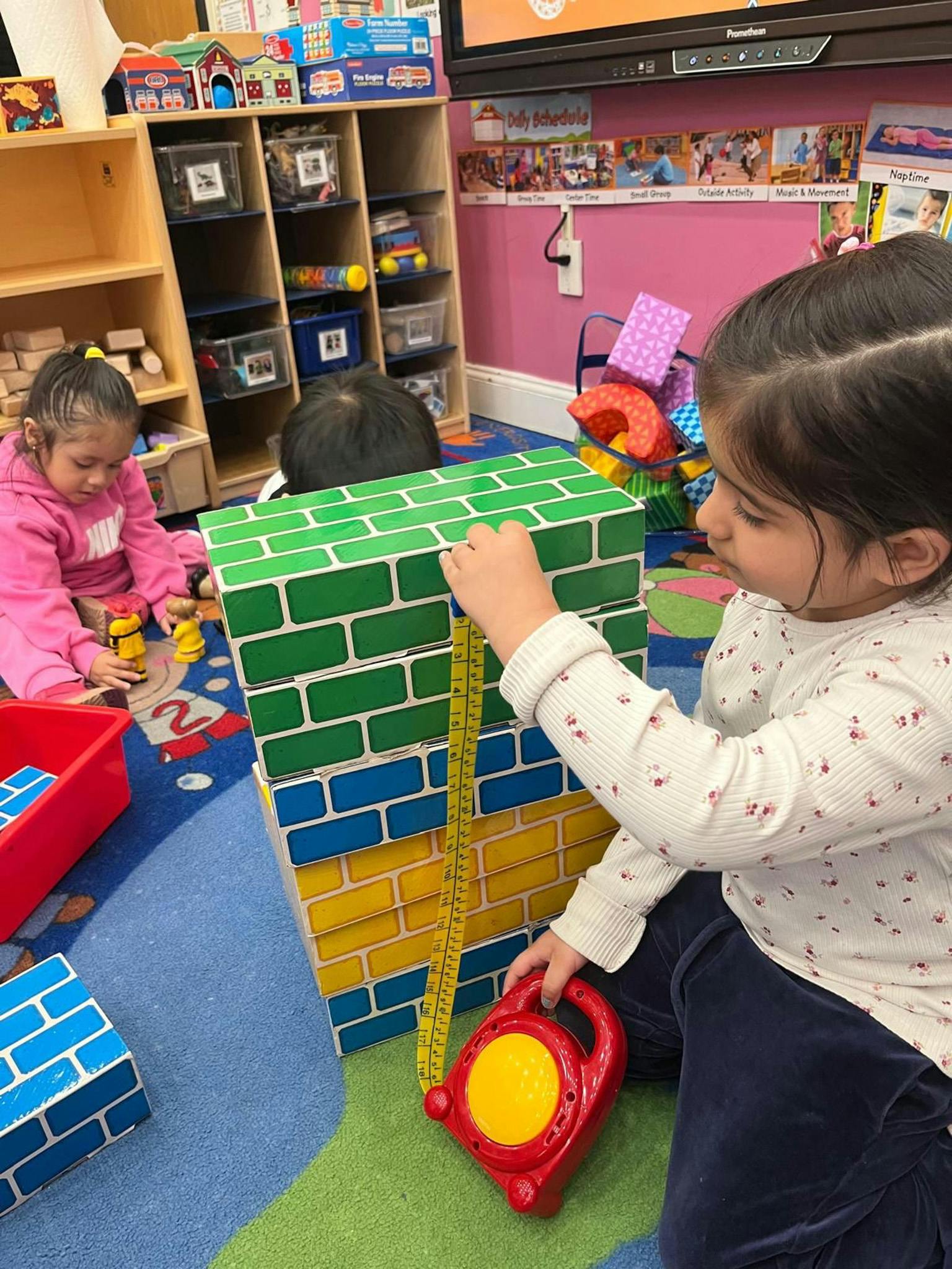 Children playing with a measuring tape and stacked blocks in a classroom