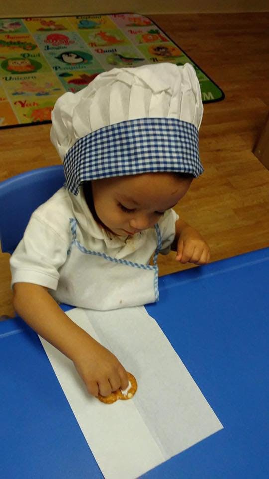 Child in chef hat and apron touching a cookie on paper