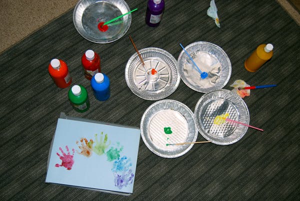 Handprints in rainbow colors on paper with paint supplies