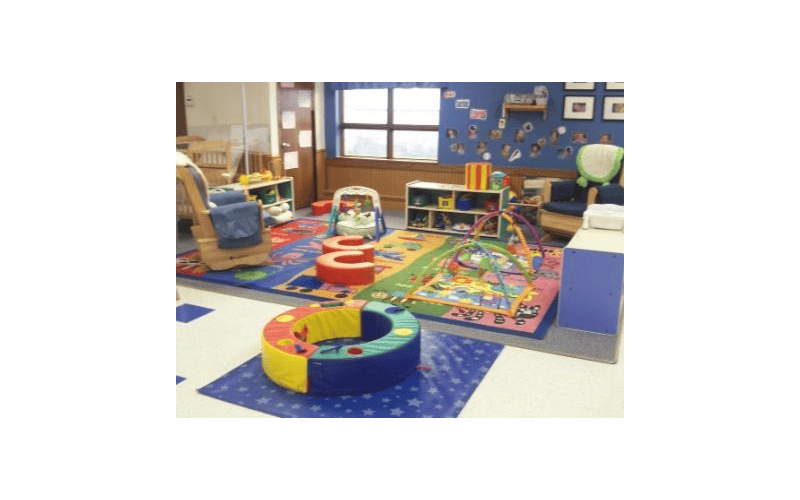 A colorful childcare room with play mats, soft seating, and toys