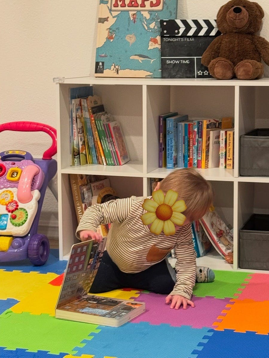 Child on colorful mat playing with a laptop-shaped book near a bookshelf