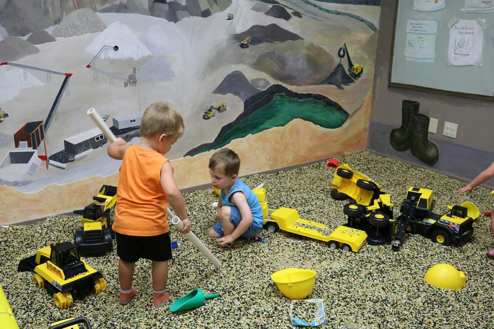 Two children playing with toy trucks and tools in a large sandbox