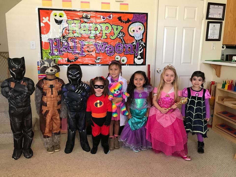 Children in Halloween costumes standing in front of a Happy Halloween banner