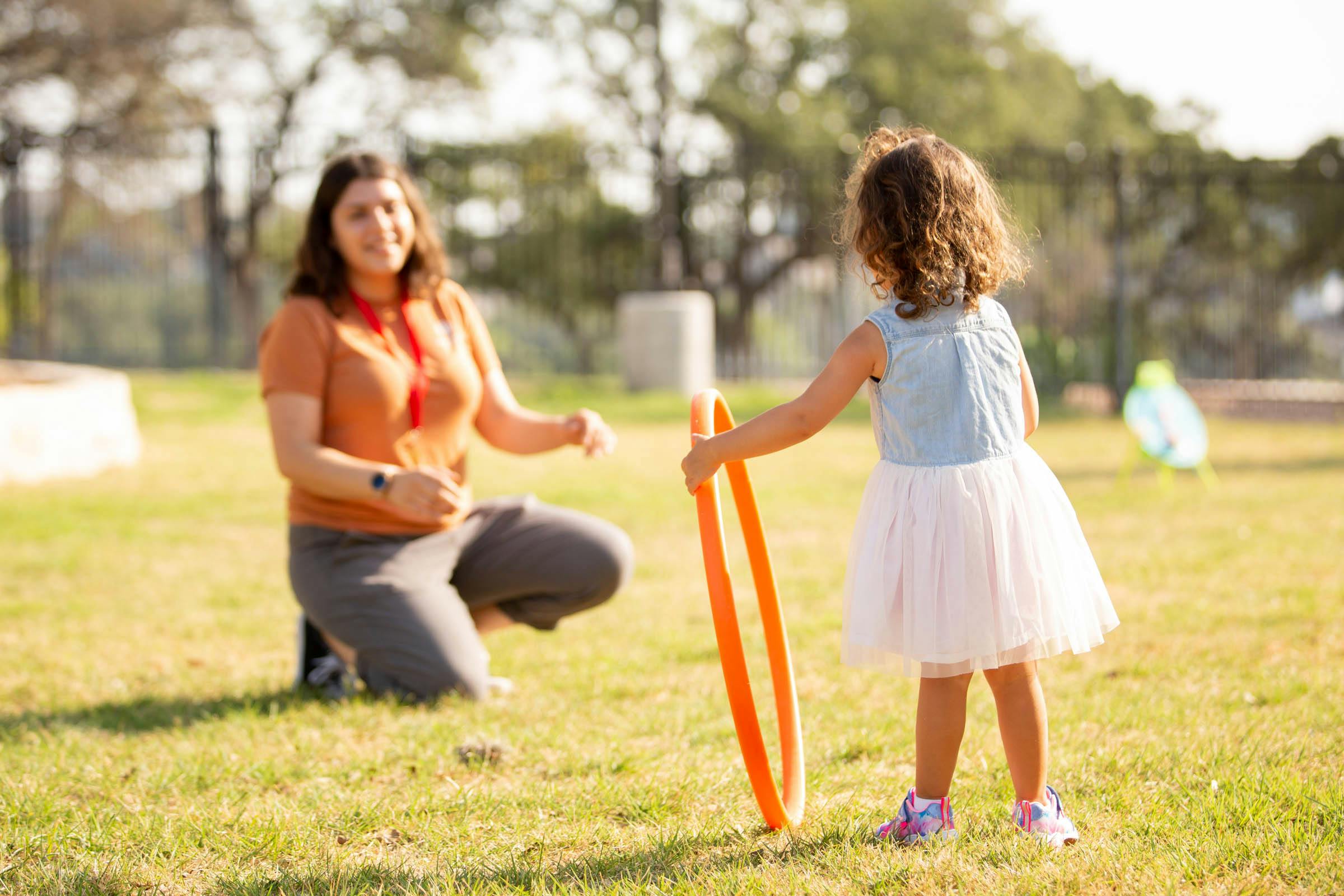 Person kneeling on grass with child holding a hoop