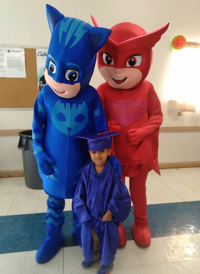 Child in graduation gown with two costumed characters