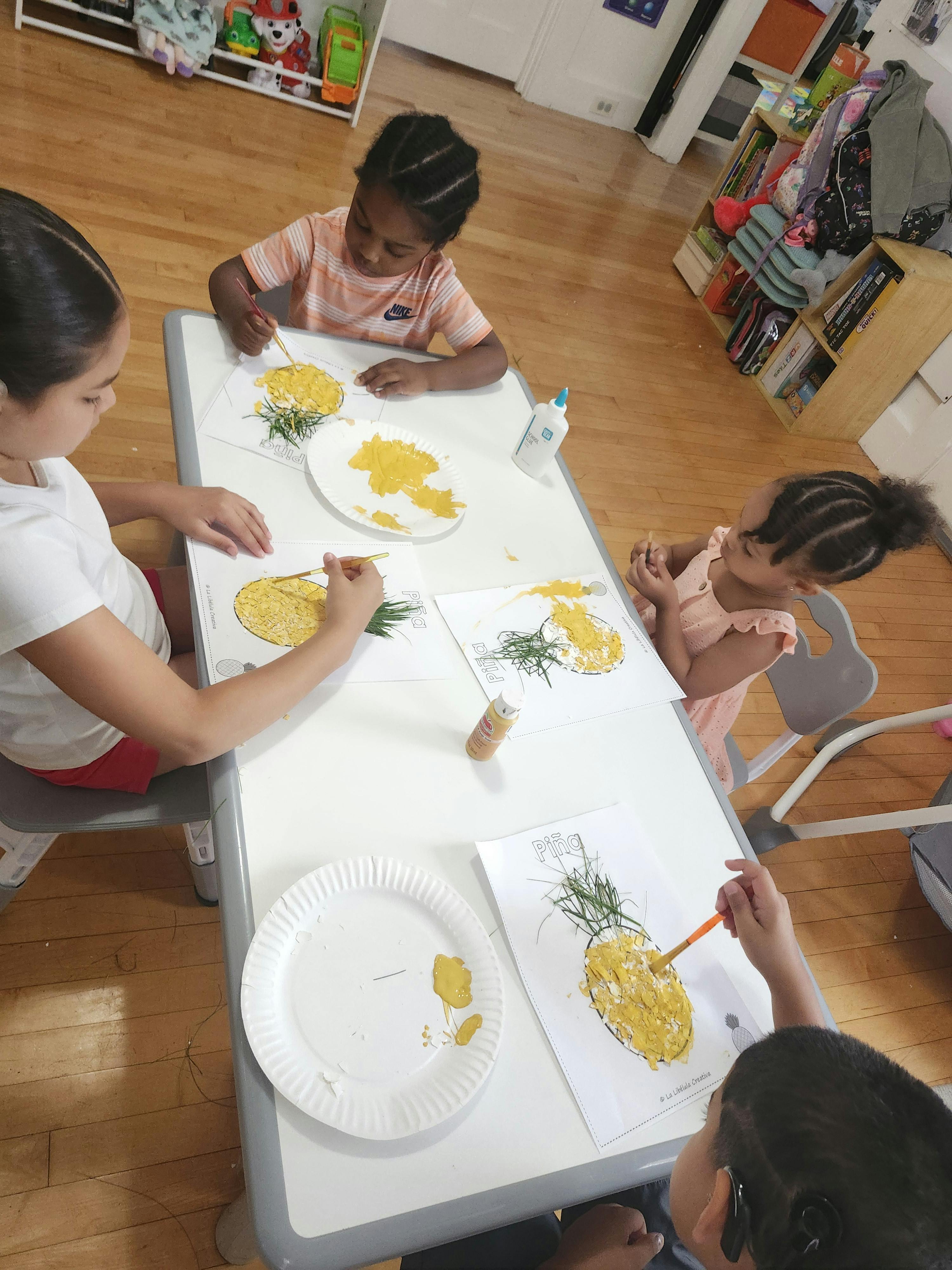 Children sitting at a table making pineapple art projects with paint and grass