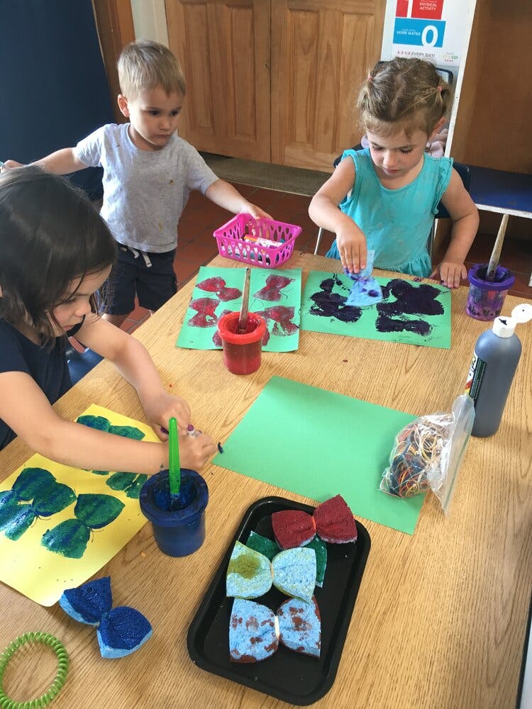 Three children painting at a table in a classroom