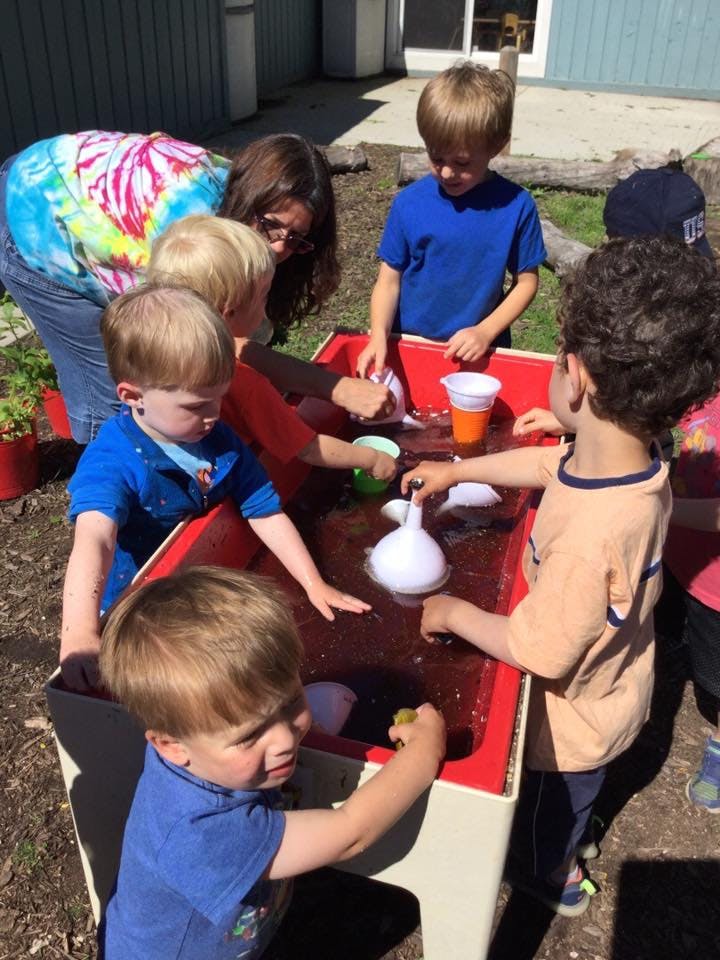 Adult and children playing at a water table outdoors