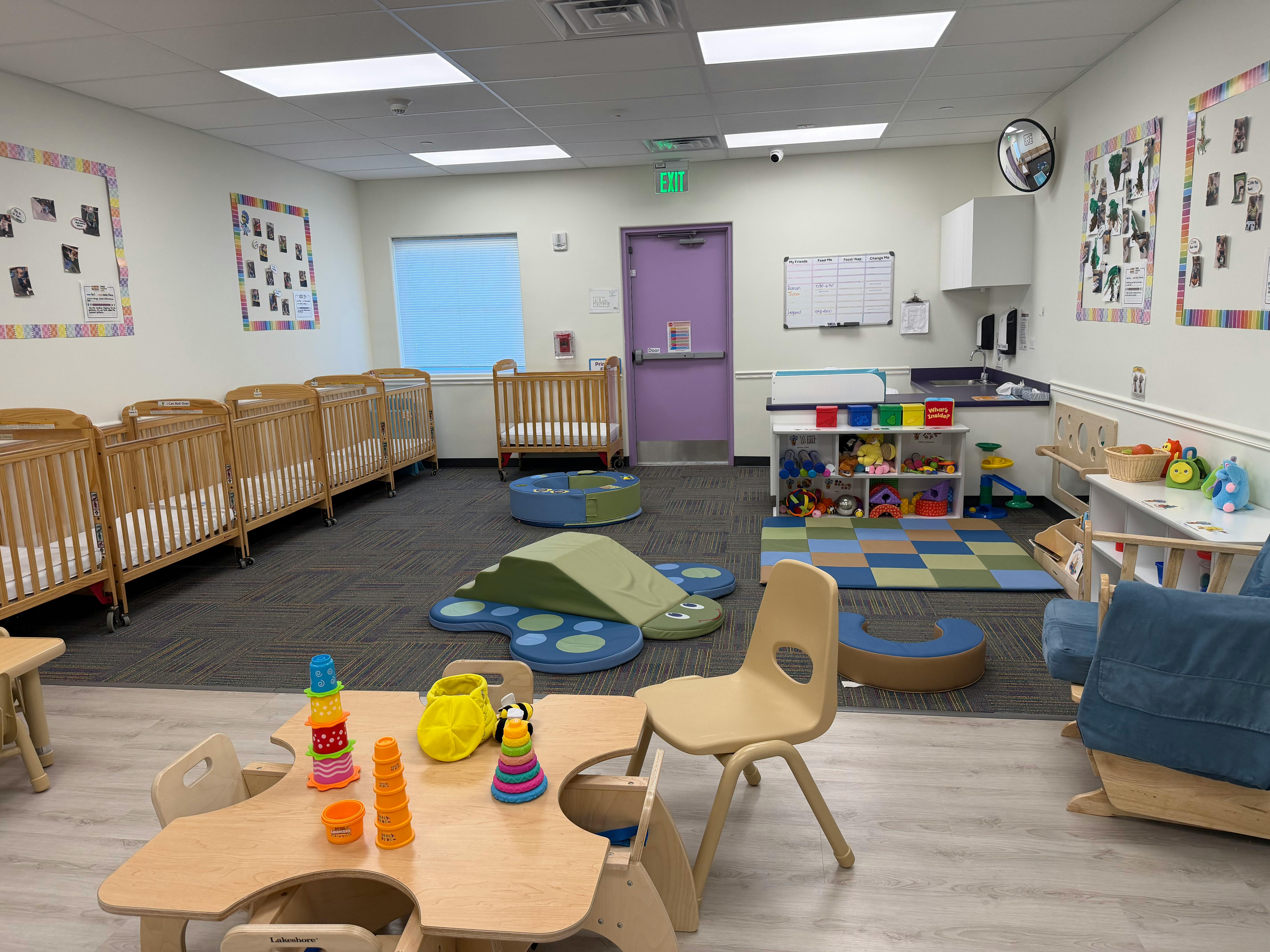 A childcare room with multiple cribs, play mats, toys, and a purple door