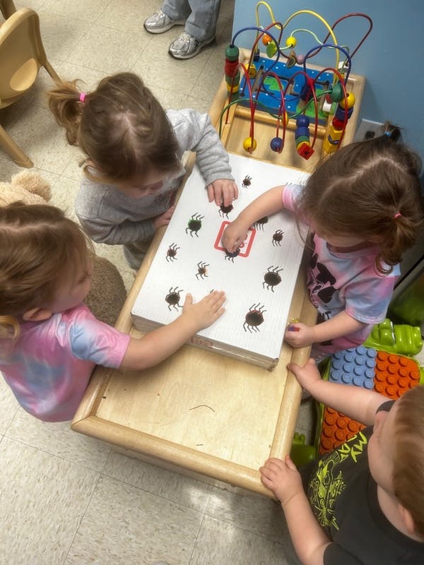Three children playing with a box covered in spider cutouts