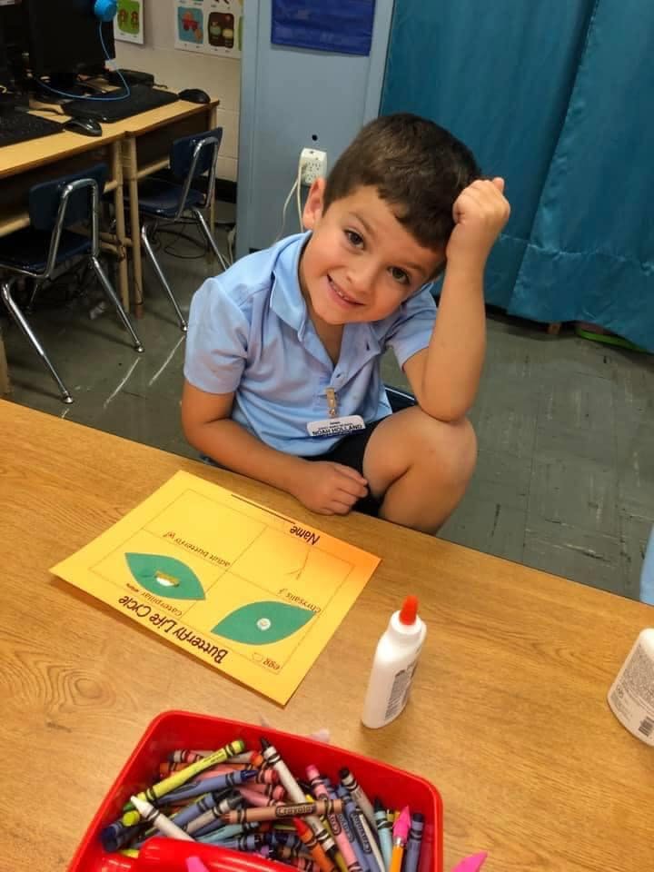 Child sitting at a desk with a craft project and crayons