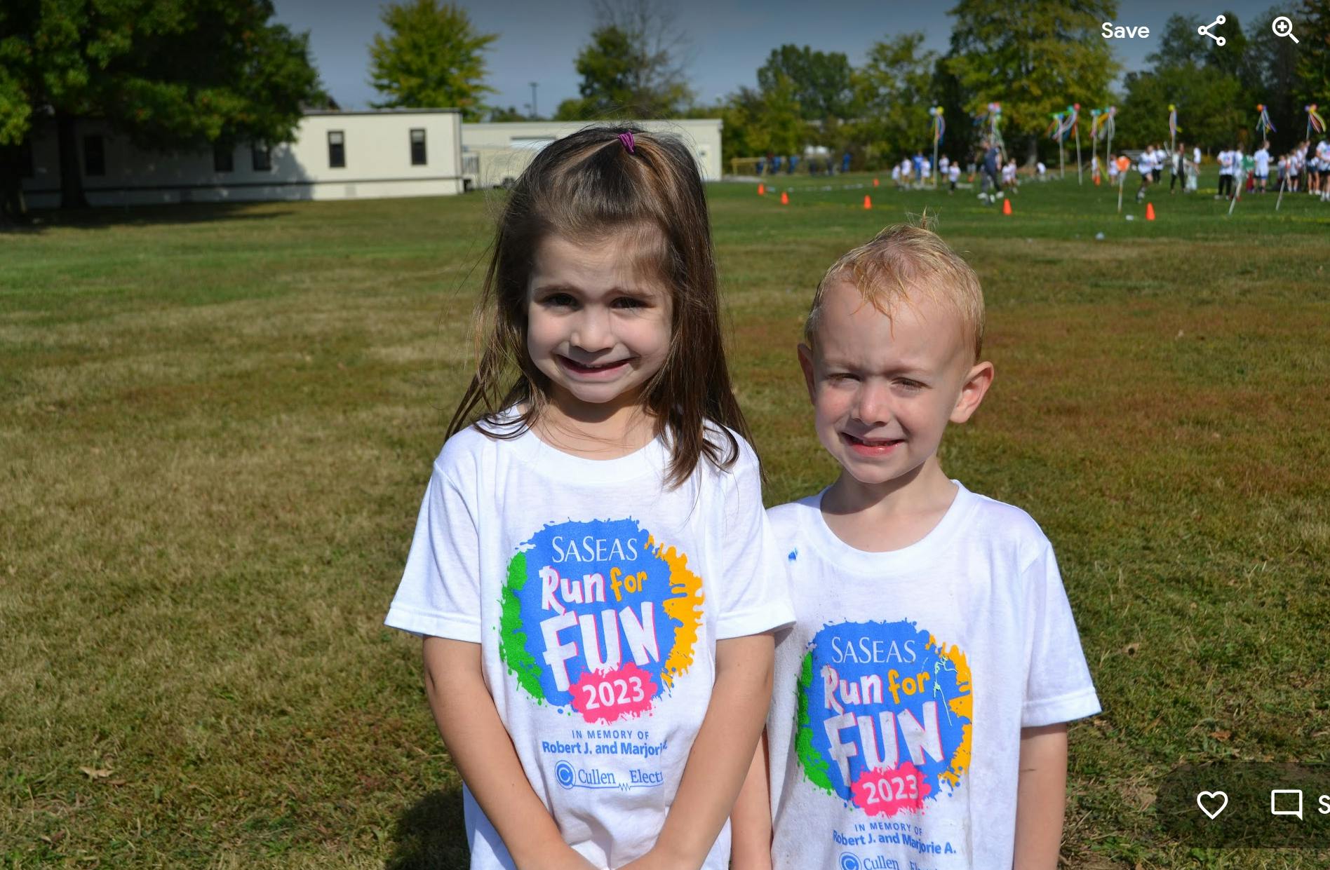 Two children in white "Run for Fun" t-shirts standing on grass