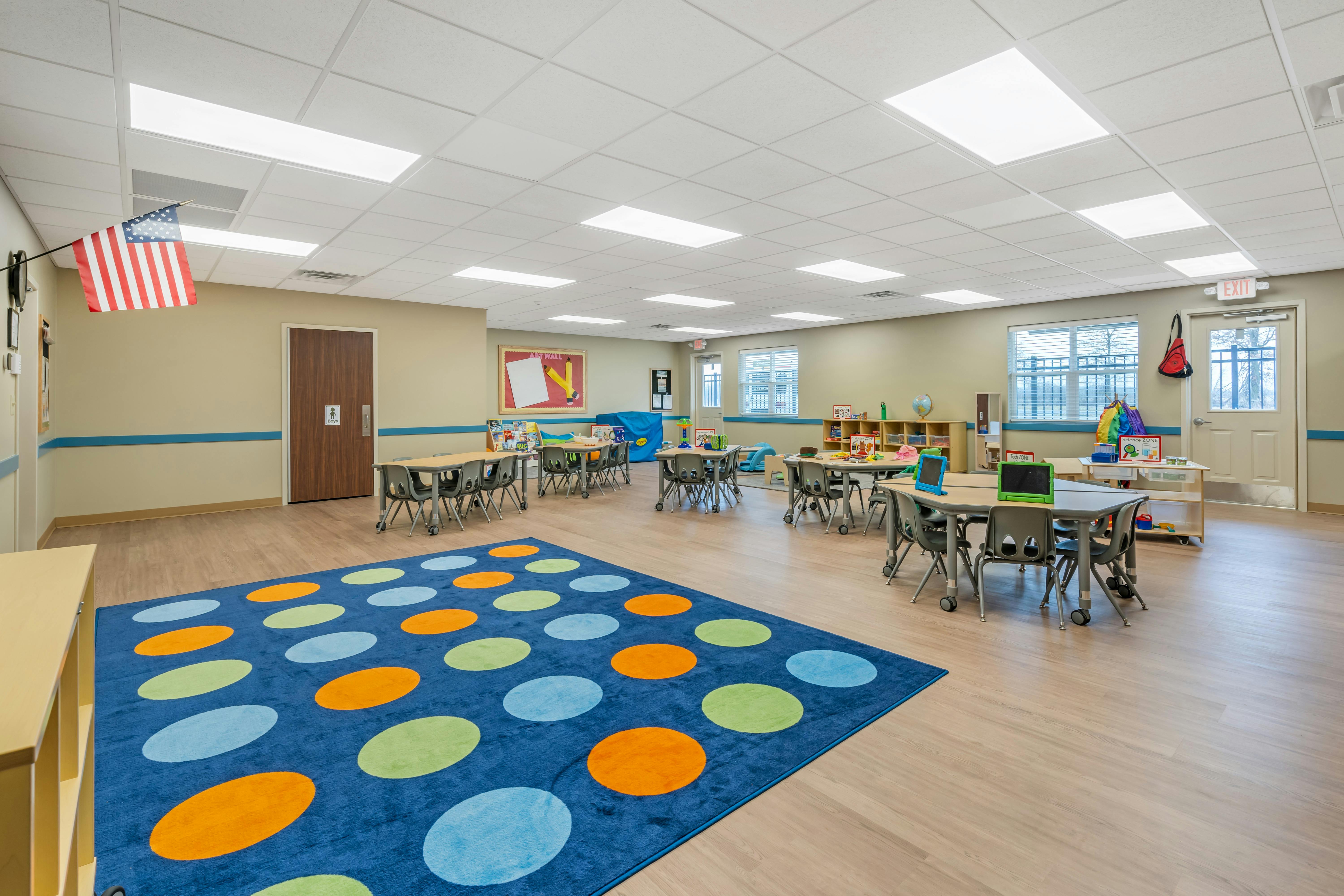 Classroom with tables, chairs, a colorful rug, and bulletin boards