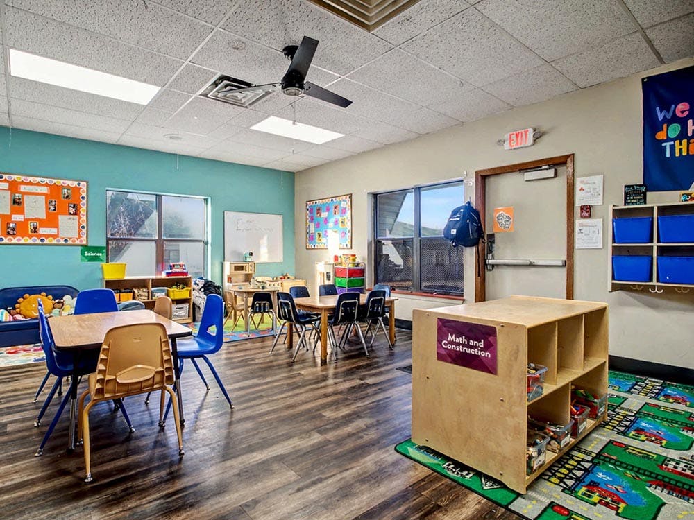 Children's classroom with small tables and chairs, a play rug, and activity centers