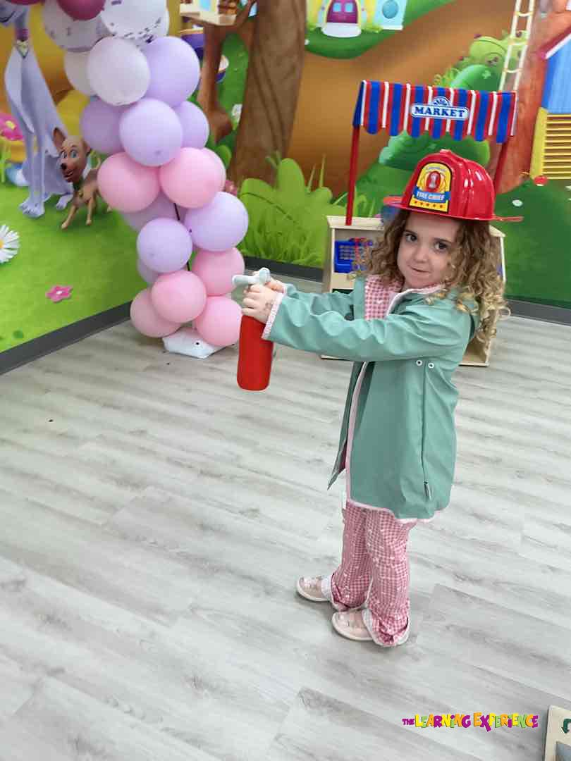 Child wearing a fire chief hat and holding a red toy fire extinguisher