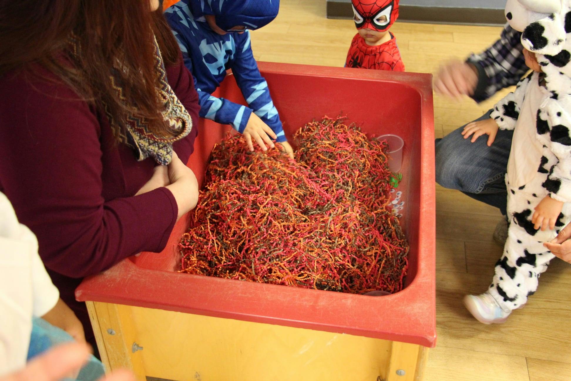 People and children playing with red shredded material in a bin