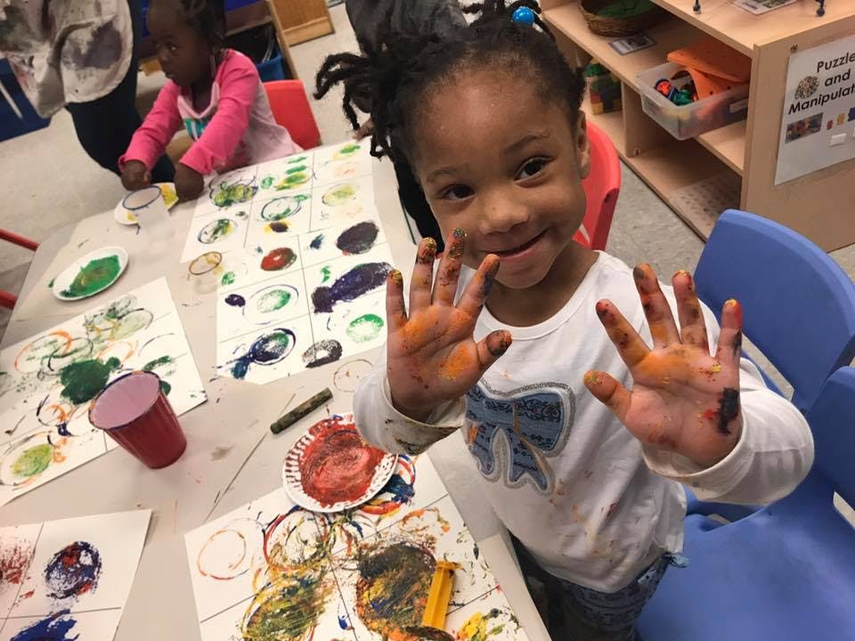 Child with paint on hands at a table with art supplies