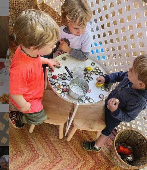 Three children playing with bottle caps at a small table