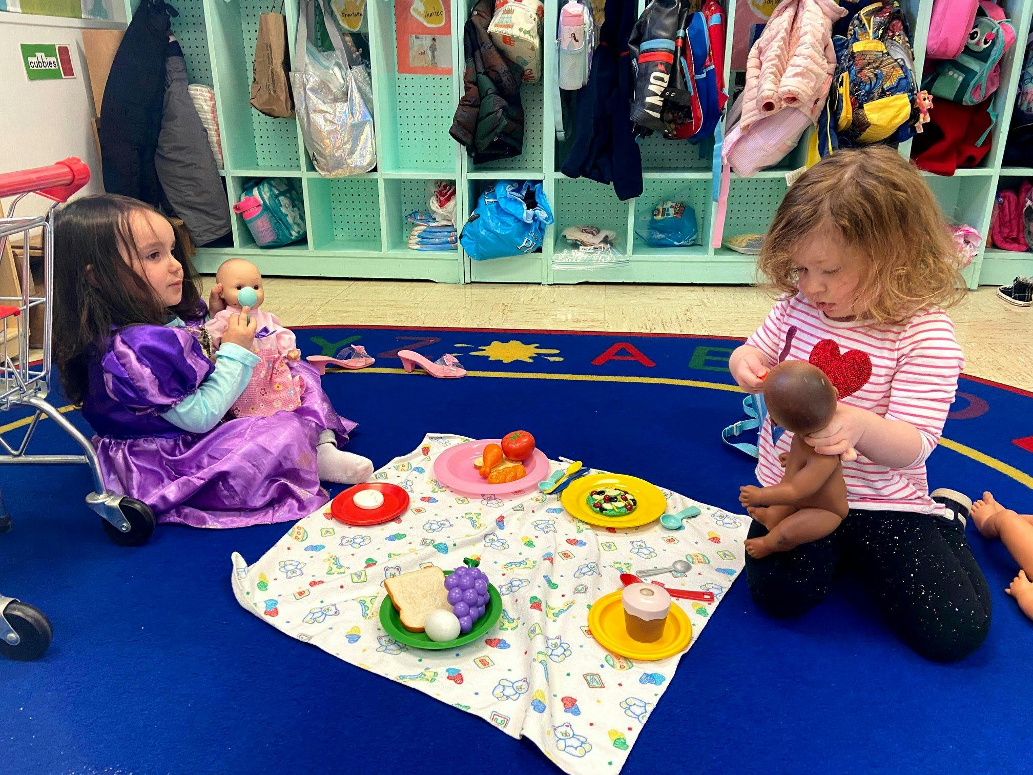 Two children playing with dolls and toy food on a blanket