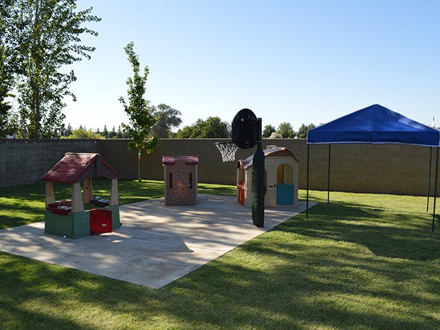 Play structures and basketball hoop on a concrete pad in a grassy yard