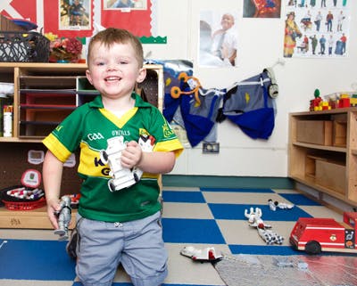 Child in a green shirt holding toys in a room with a checkered floor