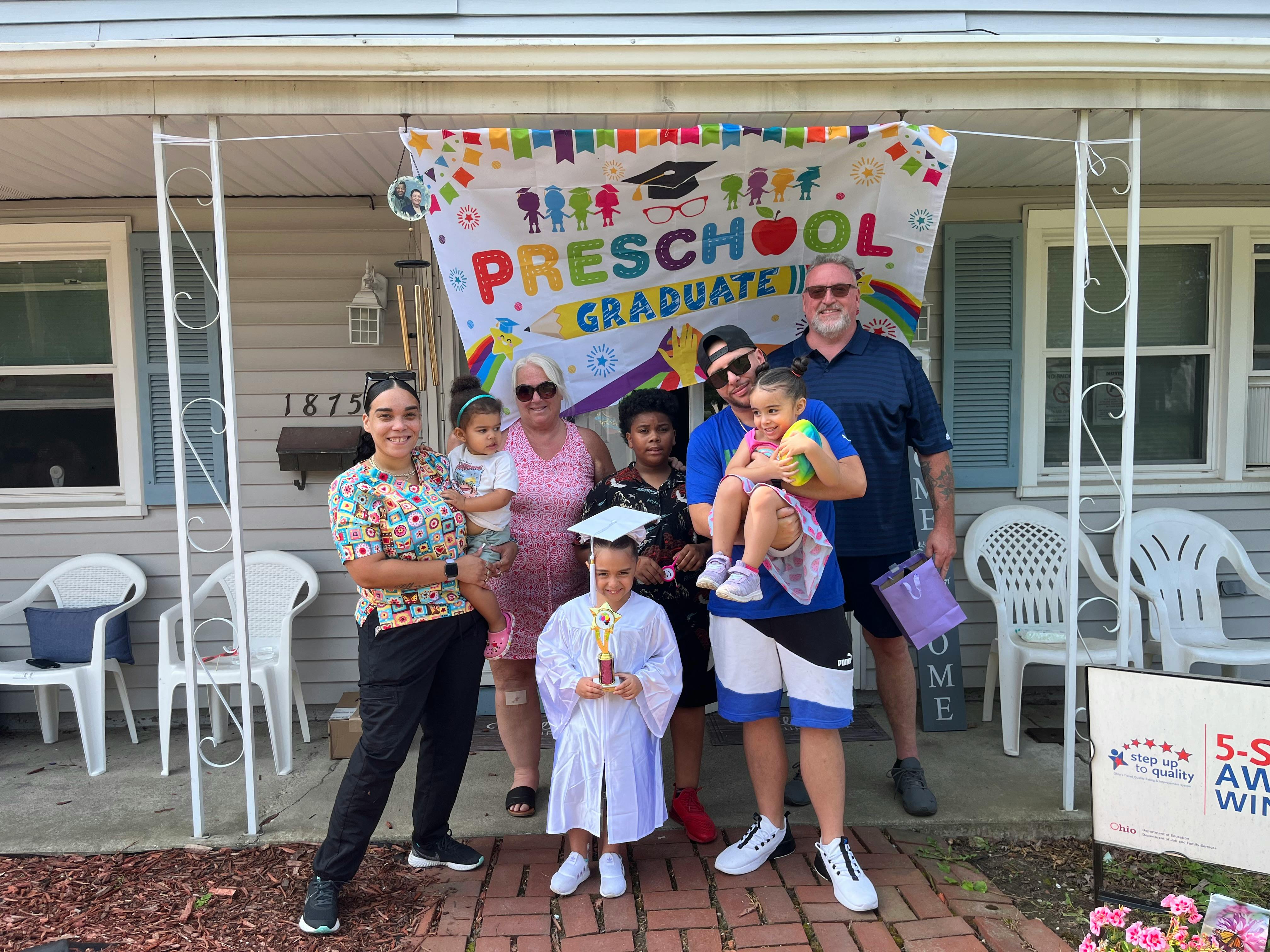 Group of people and children posing in front of a "Preschool Graduate" banner