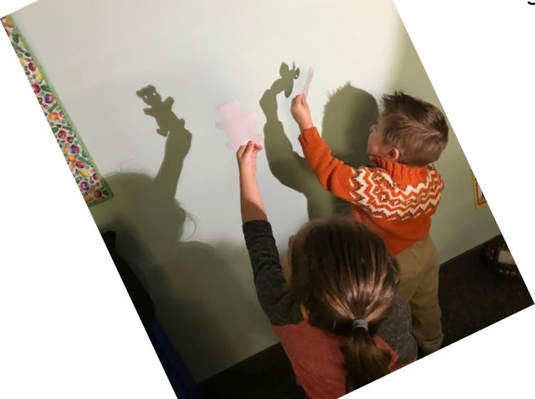 Two children holding paper cutouts creating shadows on a wall