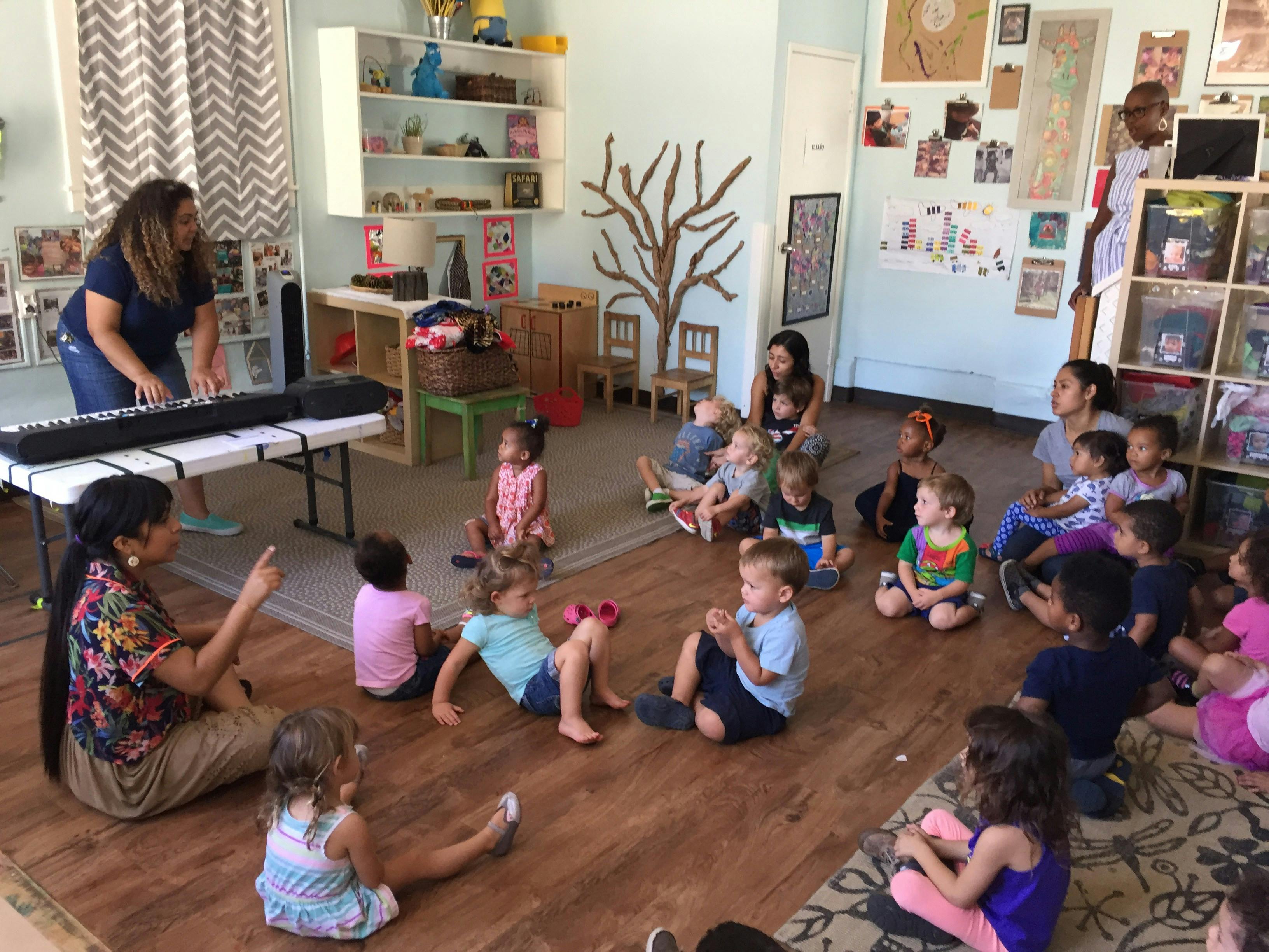 Adults and children in a classroom, some playing a keyboard