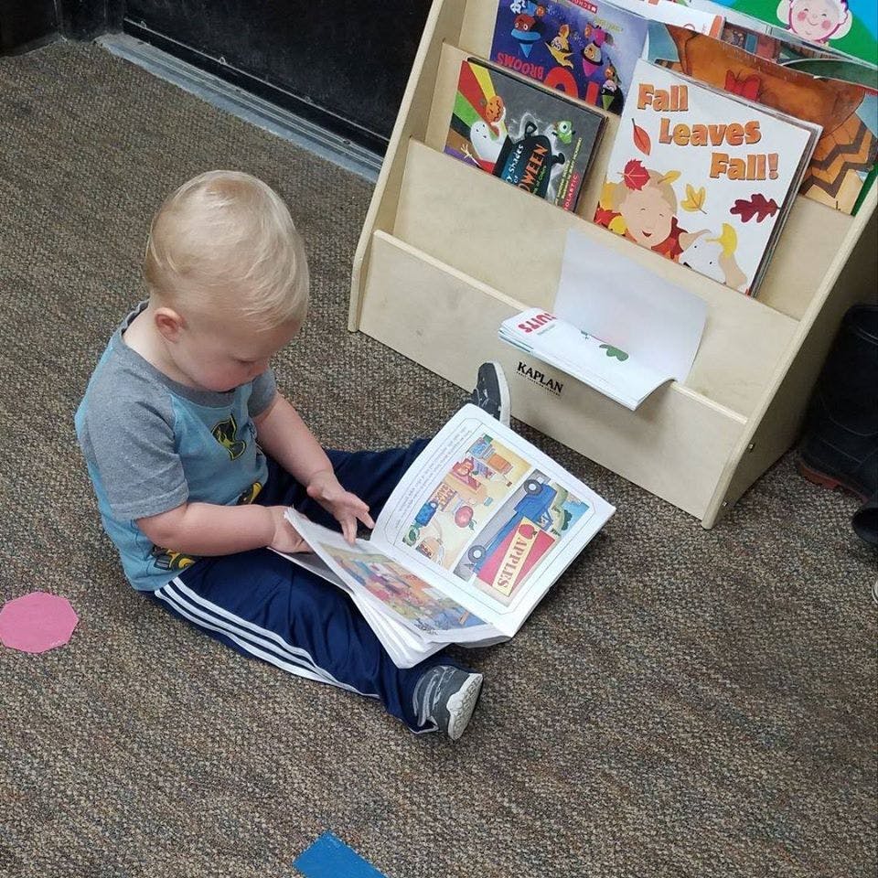 Child sitting on floor reading a book next to a bookshelf
