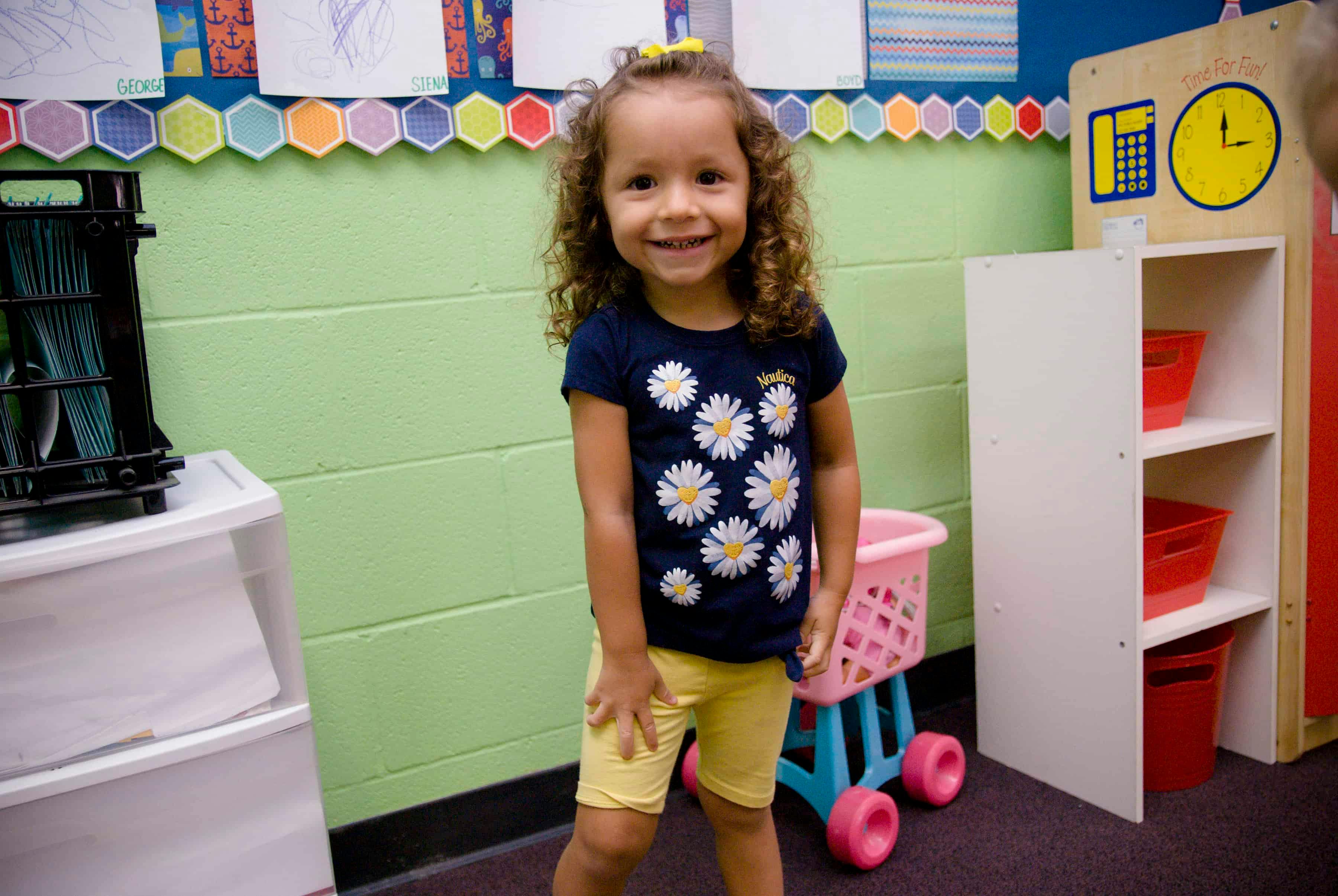 Child with curly hair standing in a classroom