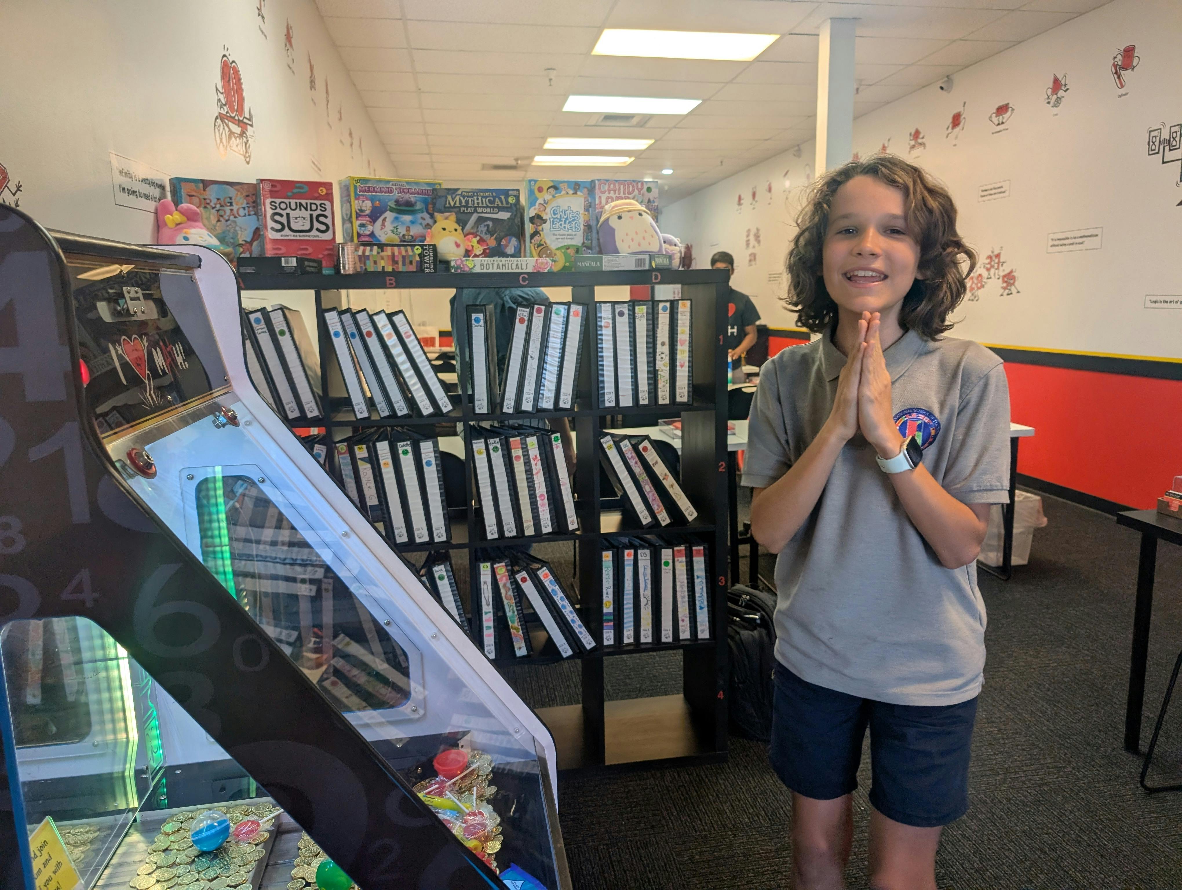 Child with hands together standing in a room with shelves of binders and an arcade game