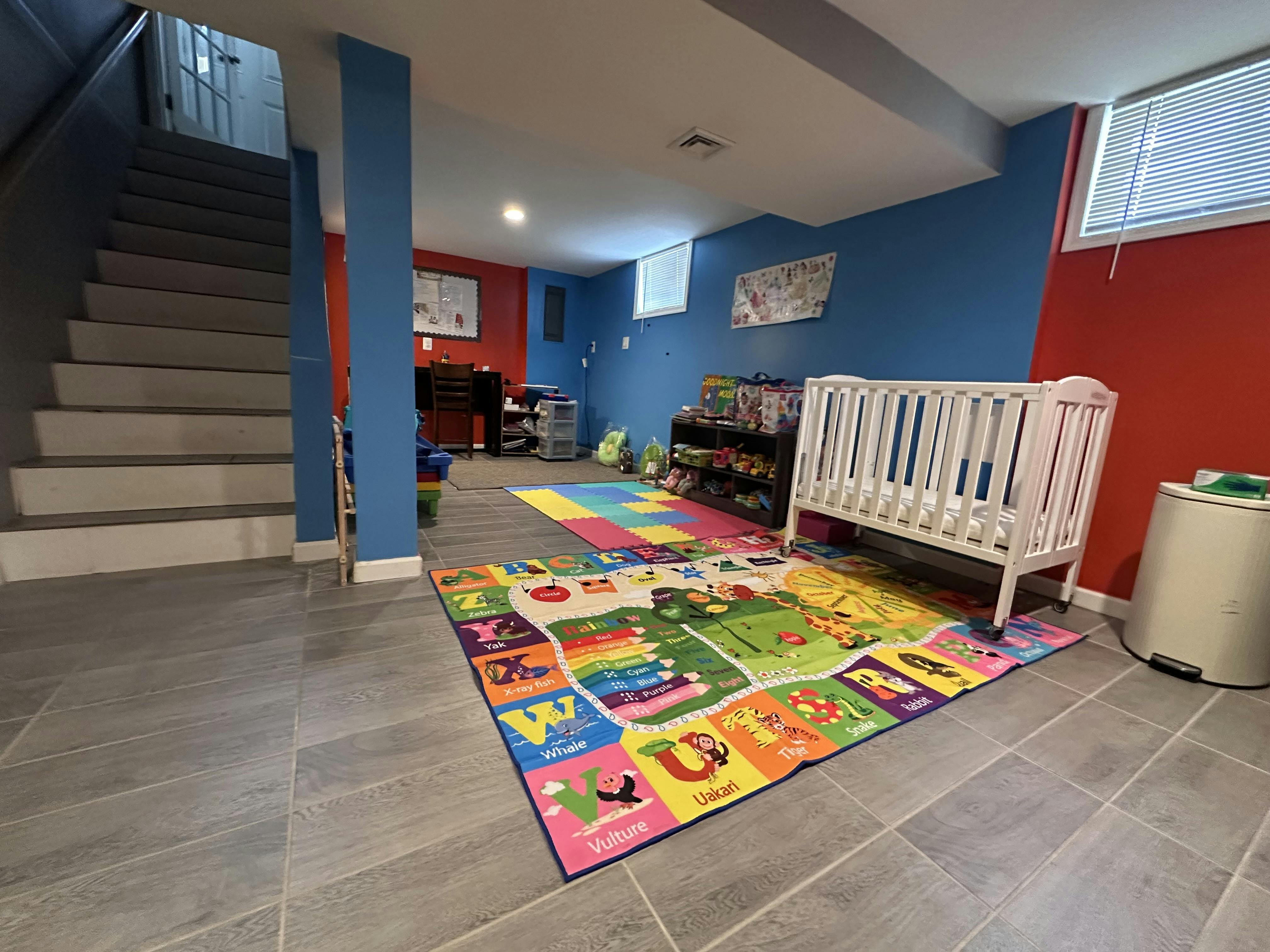 Playroom in a finished basement with colorful rugs, a white crib, and stairs