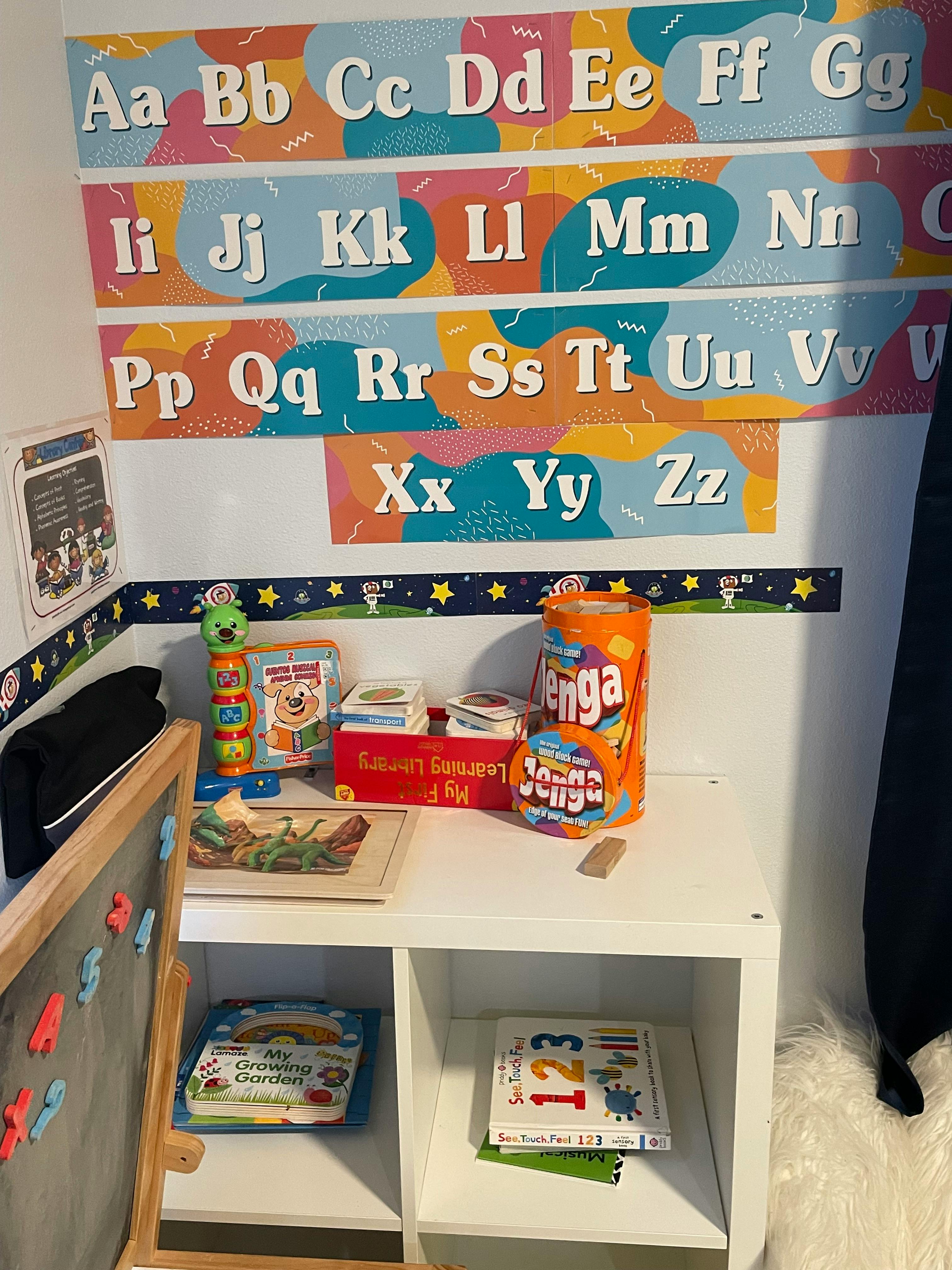 Alphabet chart on a wall above a shelf with toys and books