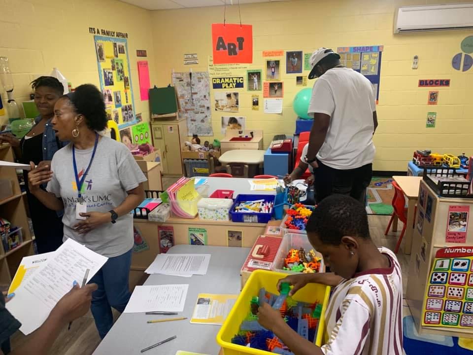 People and a child in a classroom with toys and papers