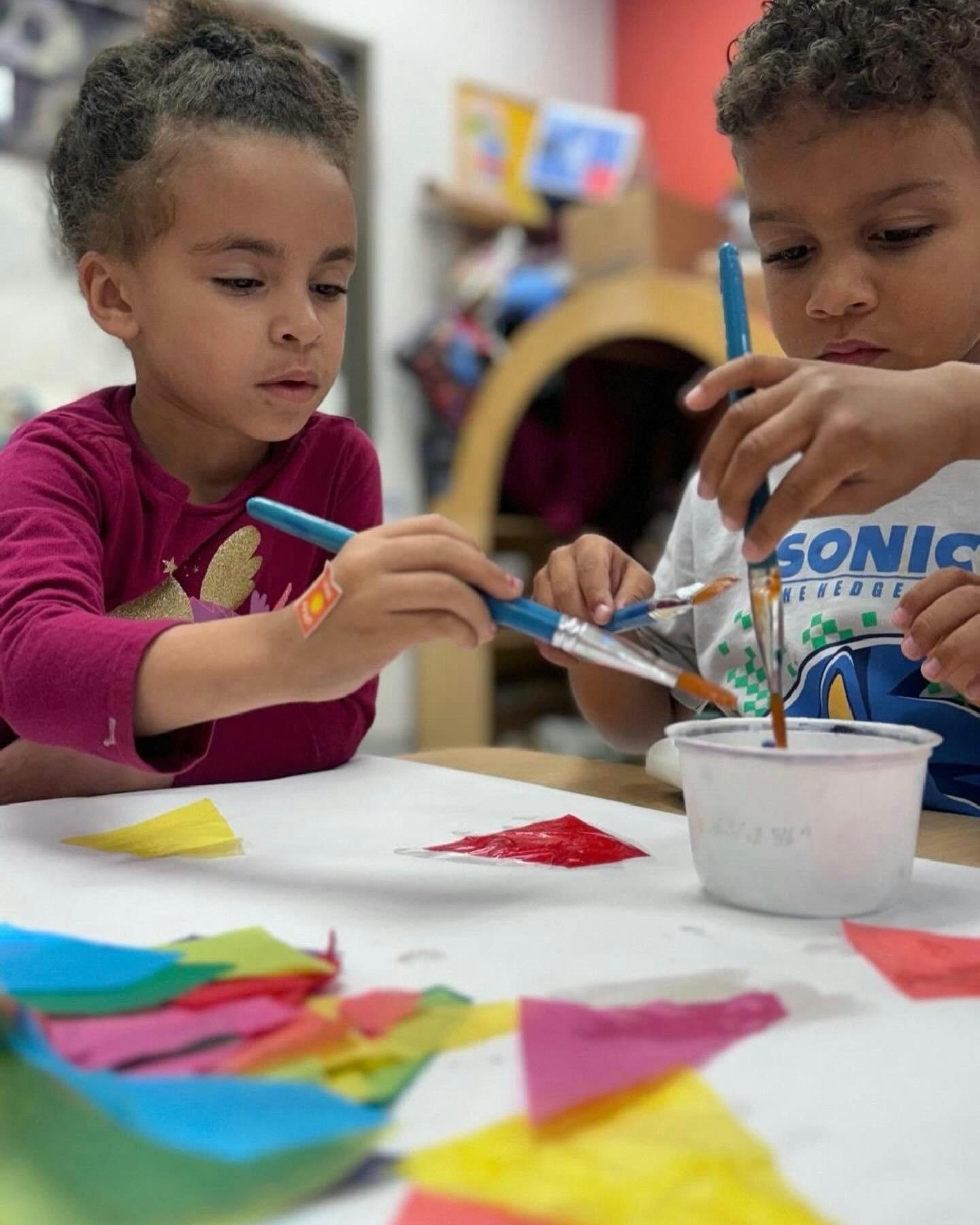 Two children painting with brushes and colorful paper on a table