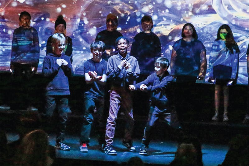Group of children and teens performing on a stage with a projected background