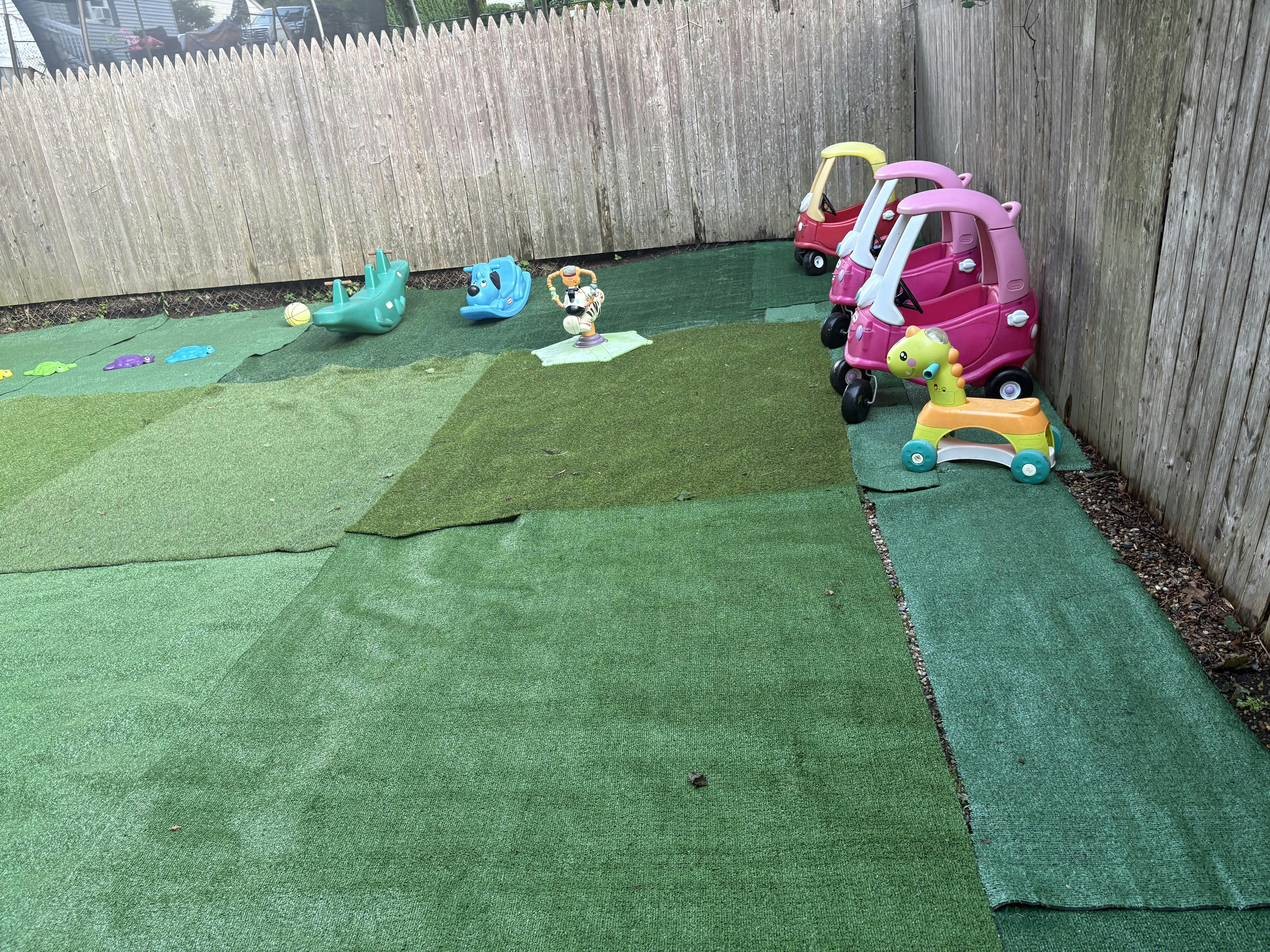 Plastic toy cars and ride-on toys on a fenced outdoor play area