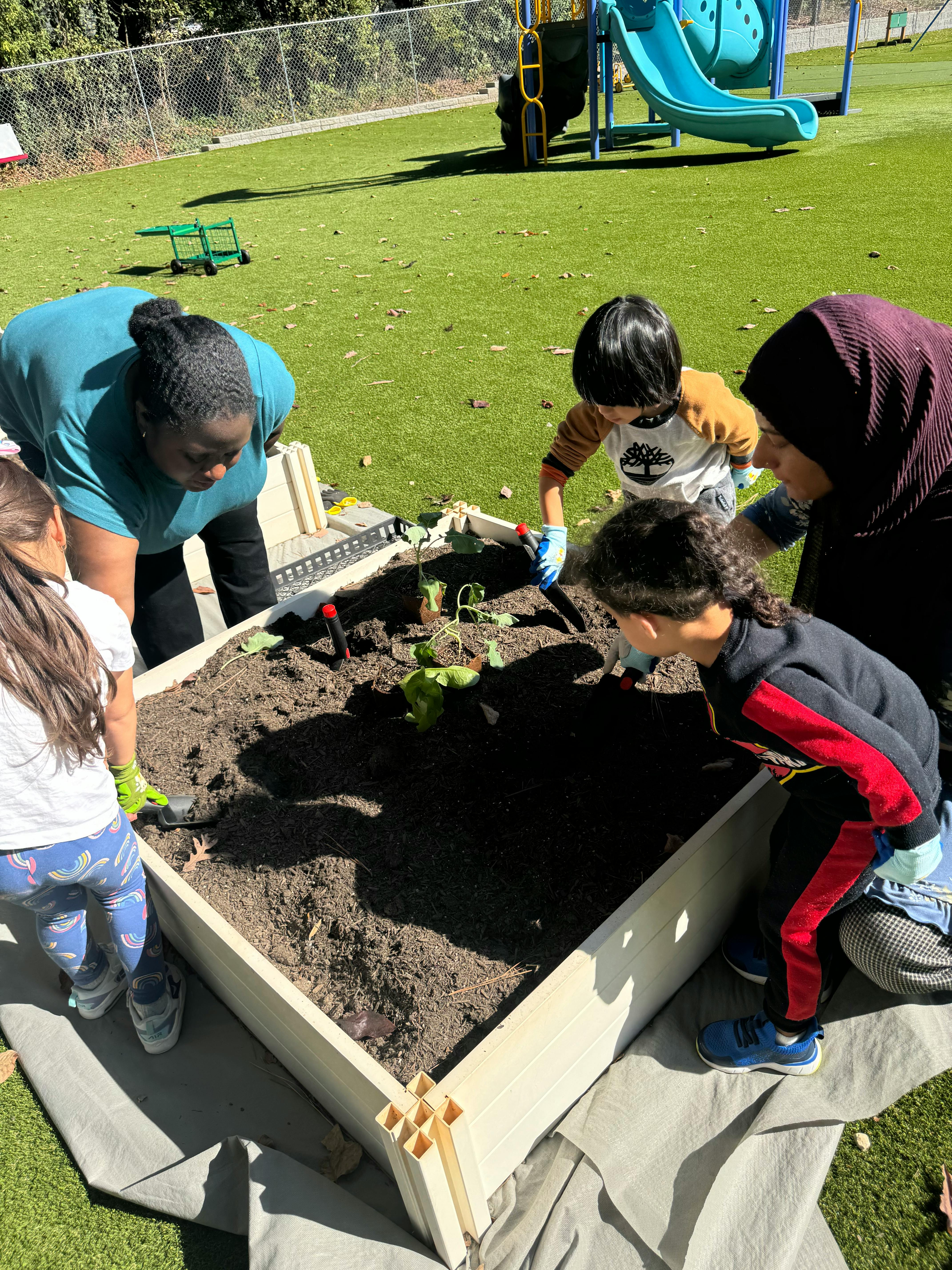 Adults and children planting in a raised garden bed outdoors