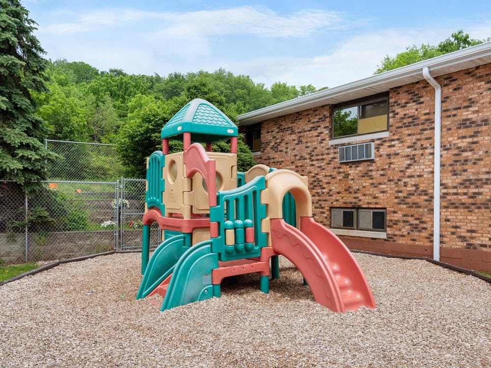 Colorful playground structure with slides on wood chips next to a brick building