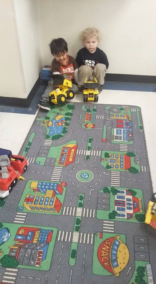 Two children playing with toy trucks on a road map rug