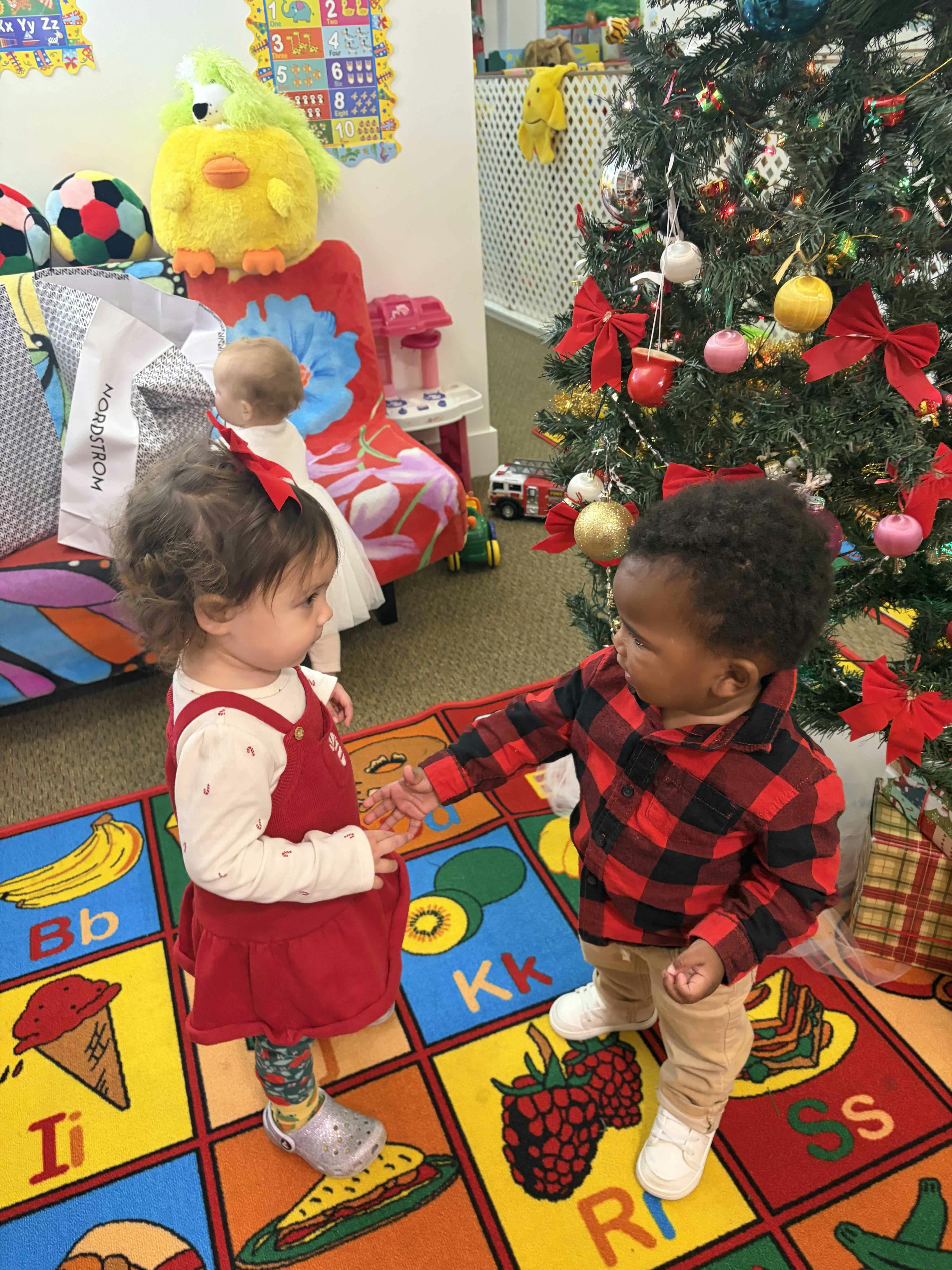 Two children standing on a colorful alphabet rug near a decorated Christmas tree