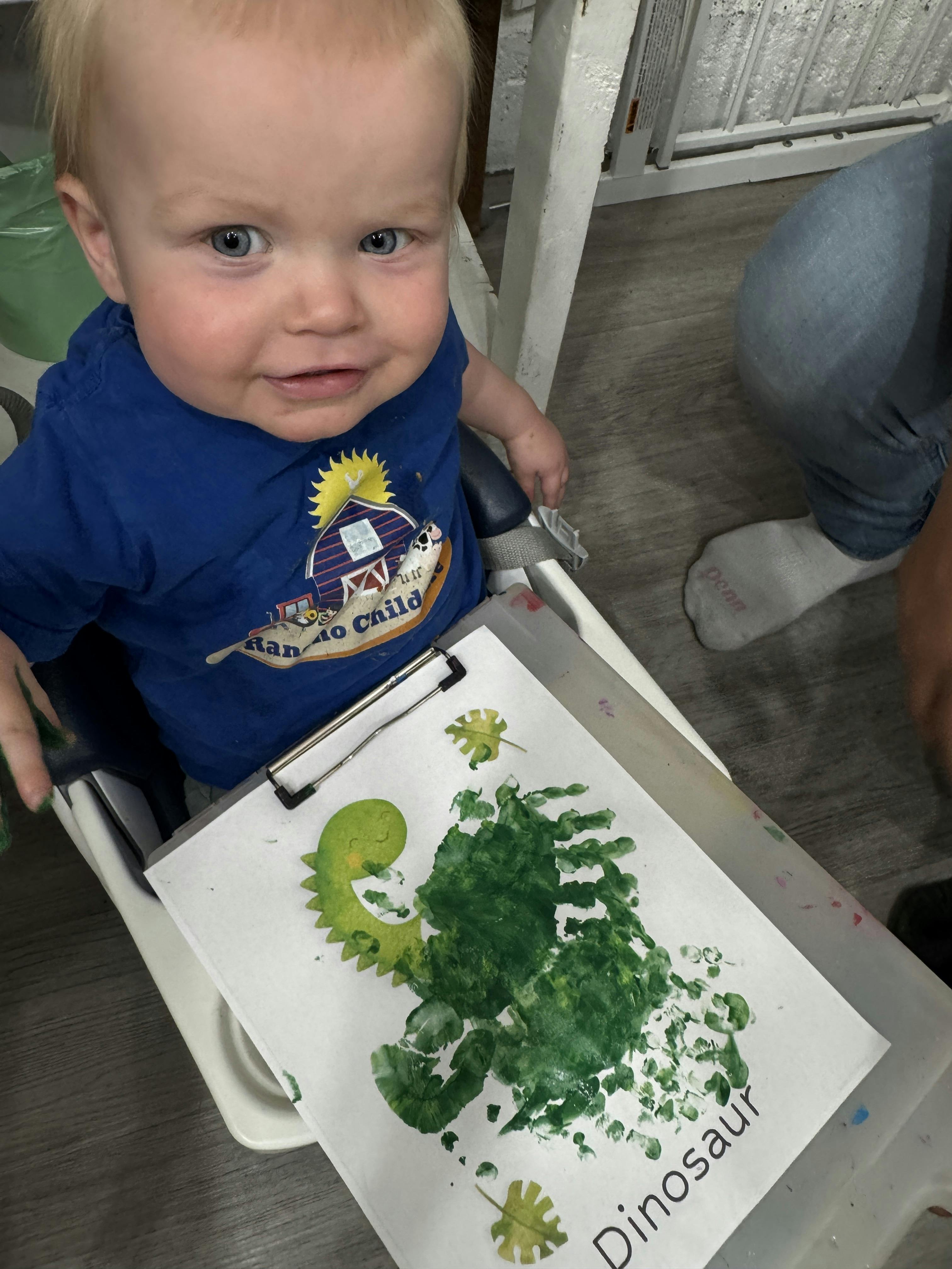 Child sitting in a high chair with a handmade dinosaur handprint craft