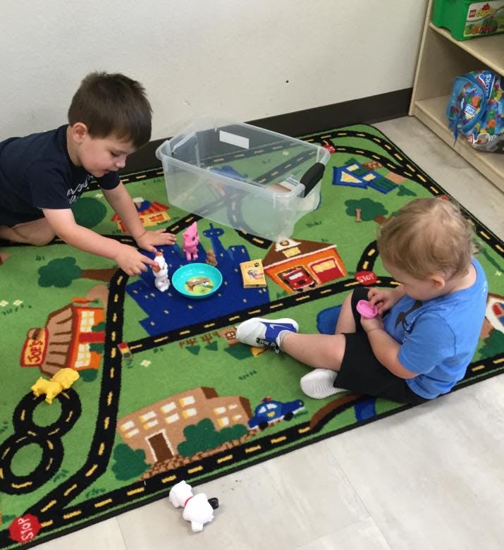 Two children playing with toys on a road map rug