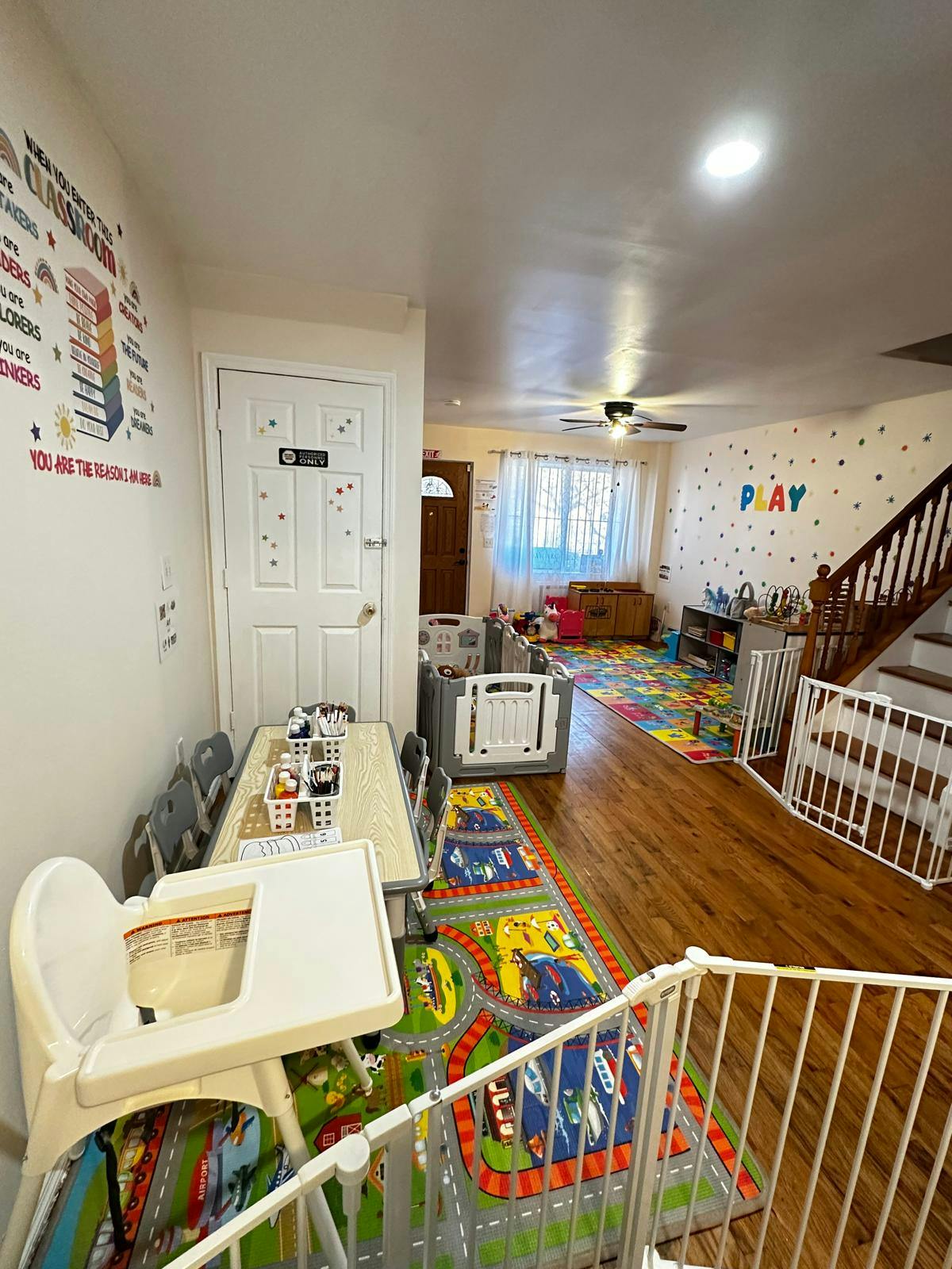 Children's play area with a colorful rug, high chair, and safety gates